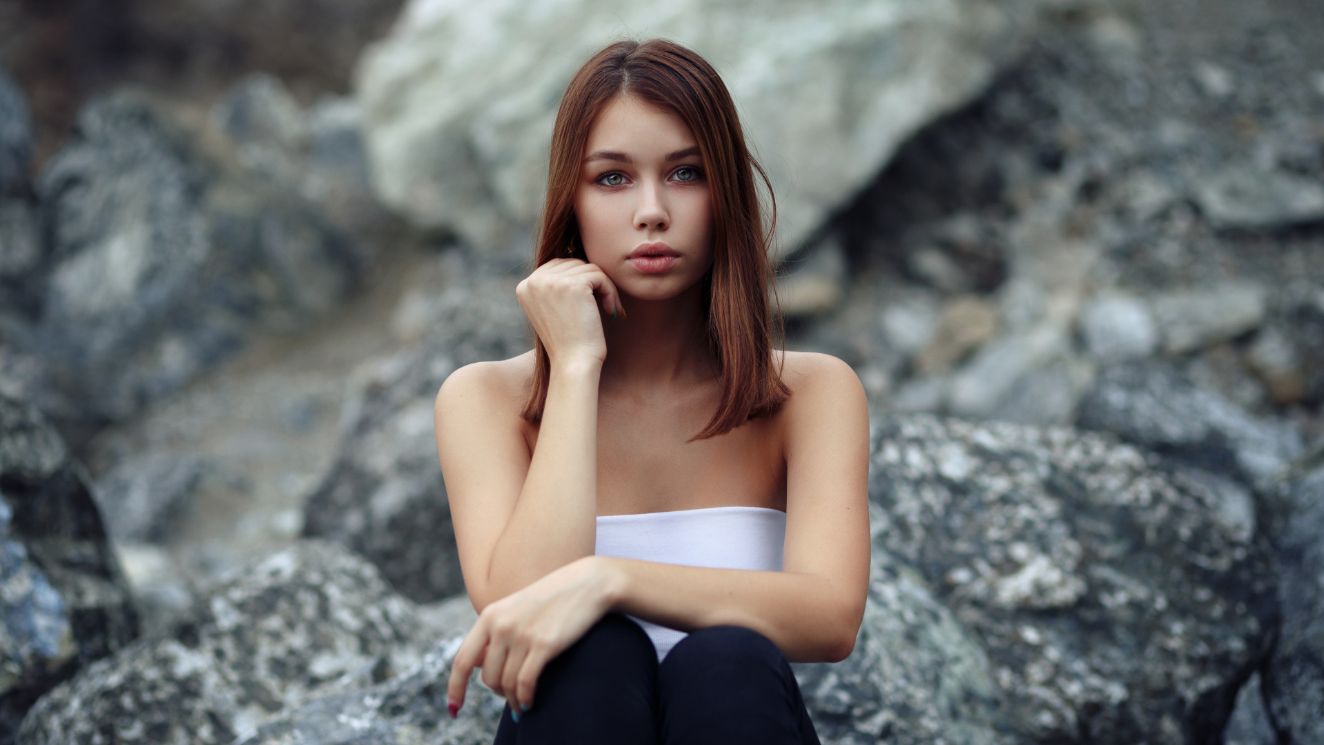 Молодая девушка сидит на камнях 