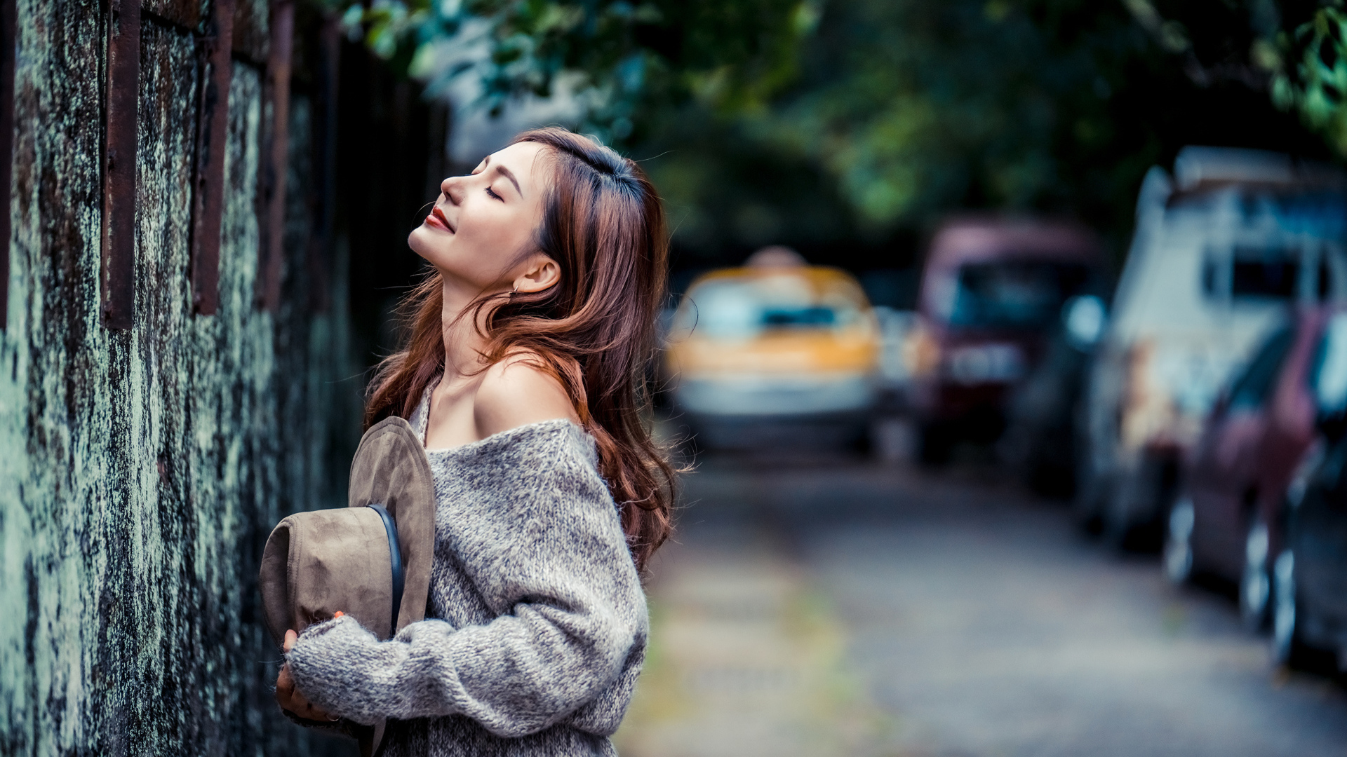 Девушка азиатка в теплом свитере стоит у забора