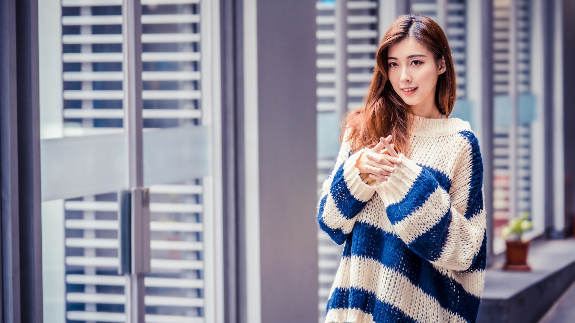 Девушка азиатка в теплом свитере стоит у окна