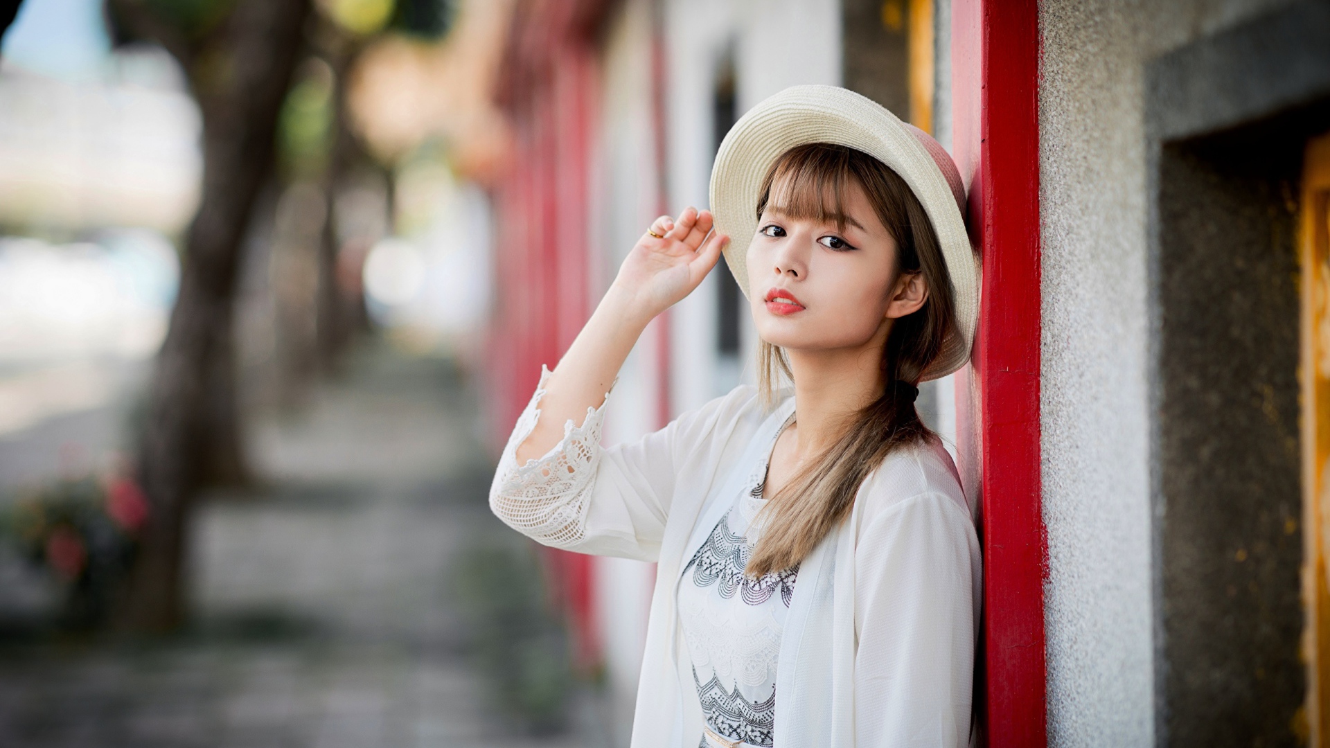 Красивая азиатка в шляпе стоит у стены