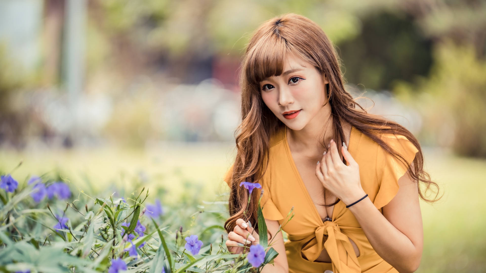 Красивая девушка азиатка в желтом платье у фиолетовых цветов 