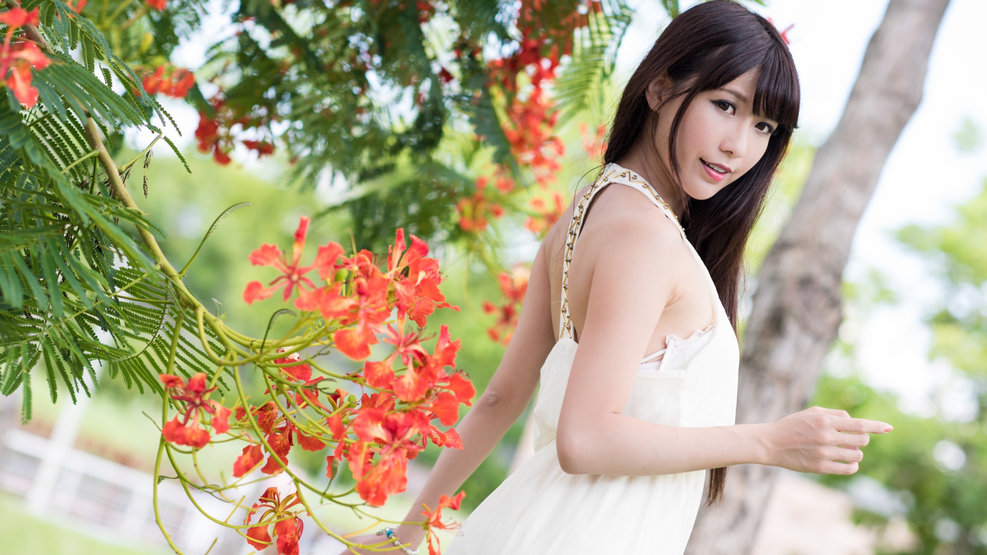 Красивая девушка азиатка в красном платье у дерева с цветами