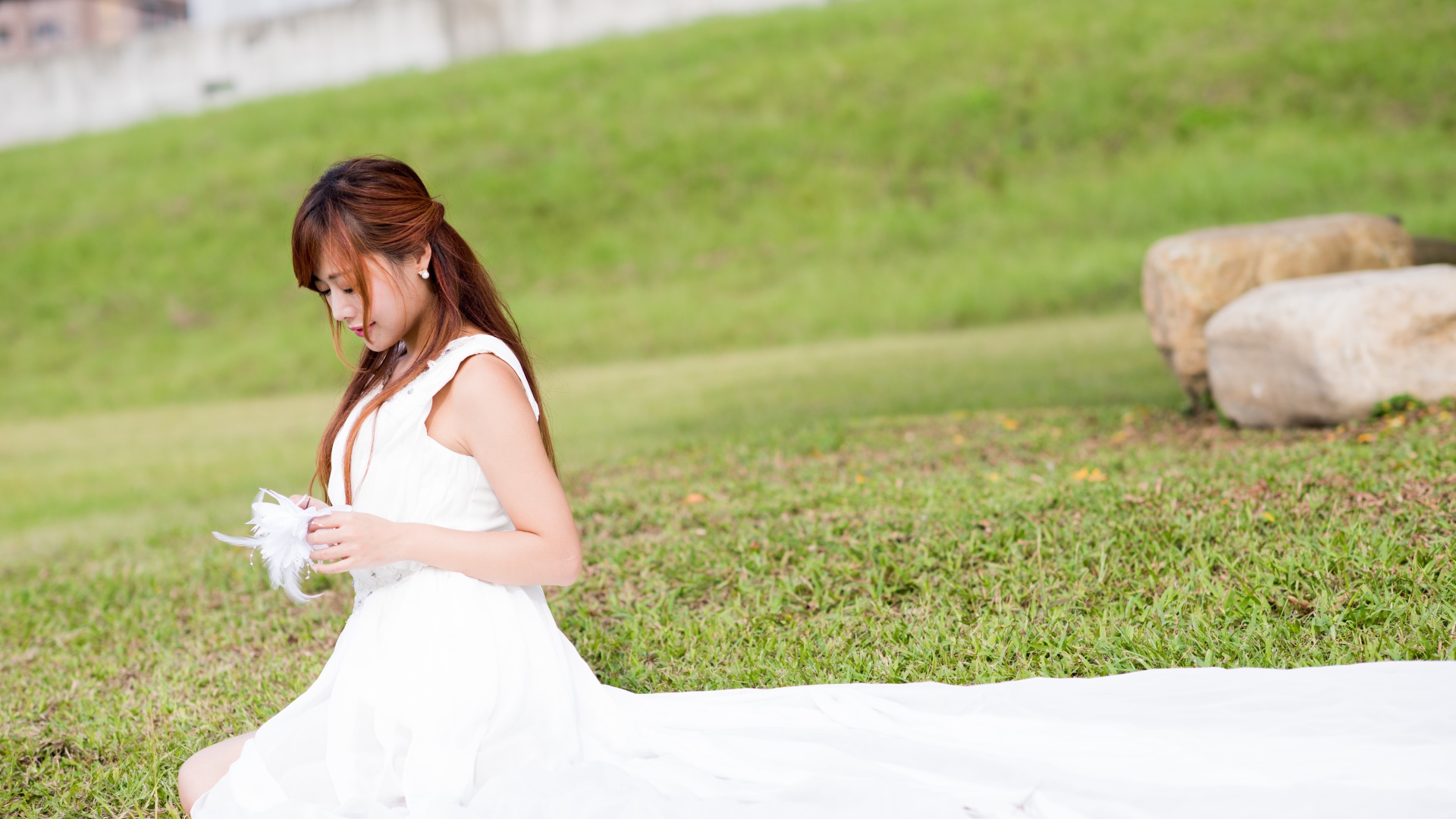 Красивая девушка азиатка в свадебном платье сидит на траве