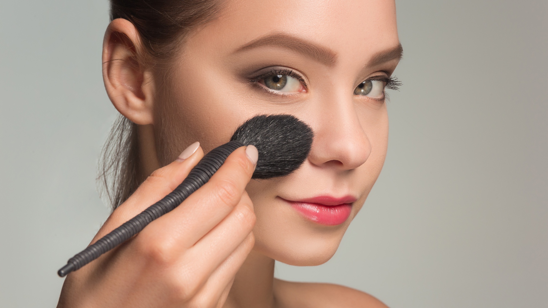 Красивой девушке наносят макияж на лицо кистью 