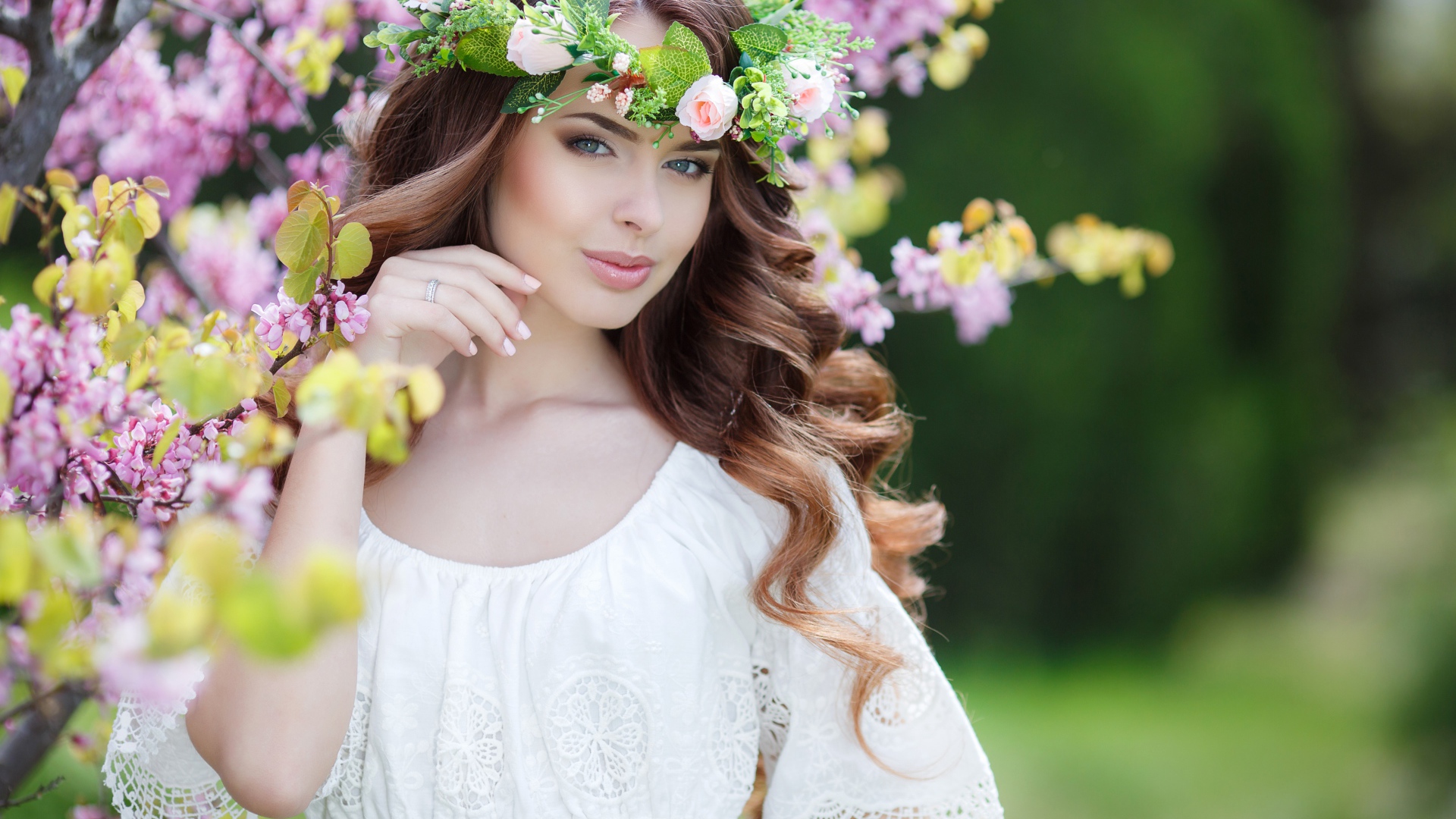 Красивая девушка в белом платье с венком на голове стоит у дерева 