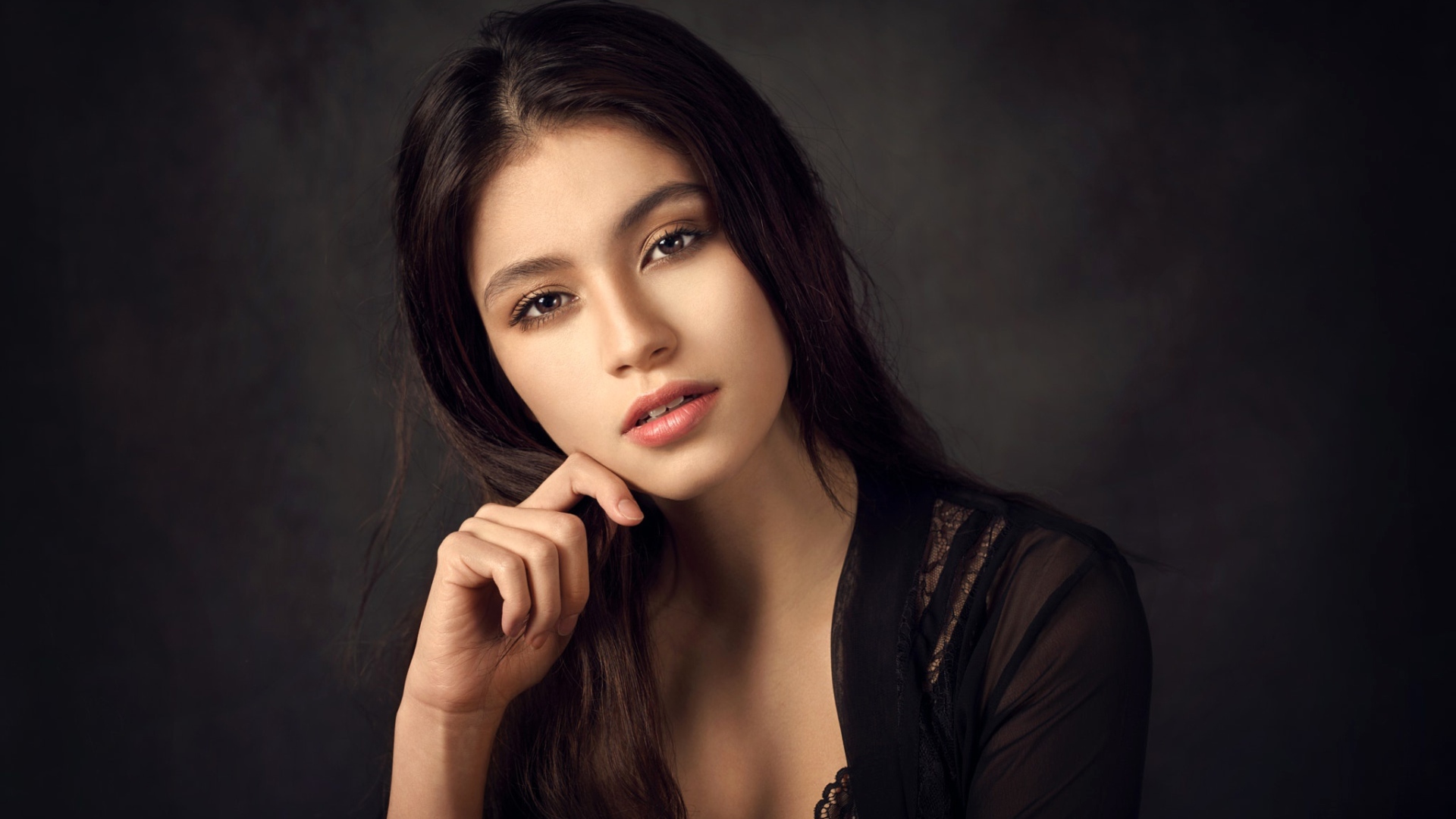 Красивая девушка в черном сидит на сером фоне