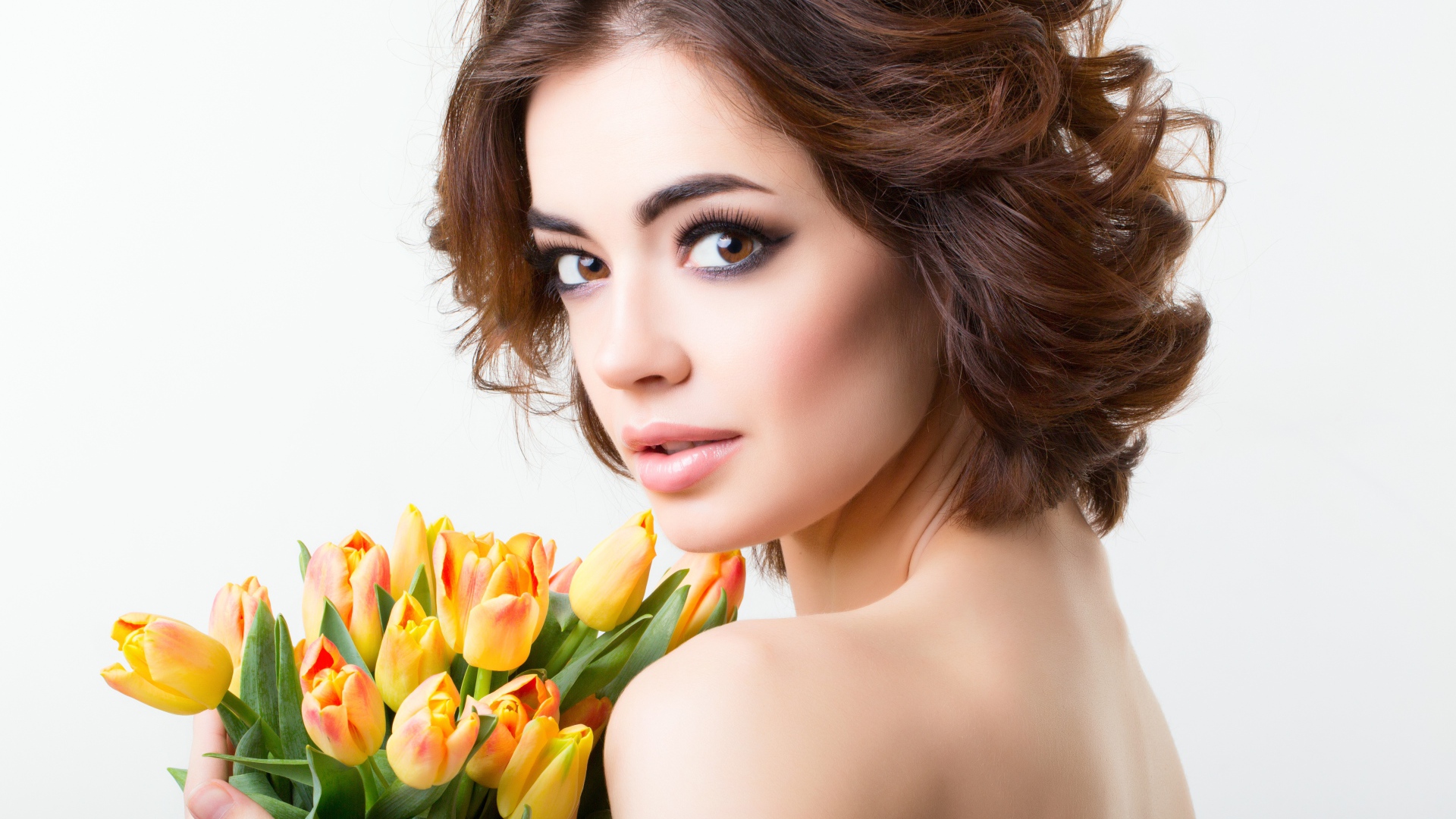 Красивая девушка с прической в букетом тюльпанов в руках на белом фоне