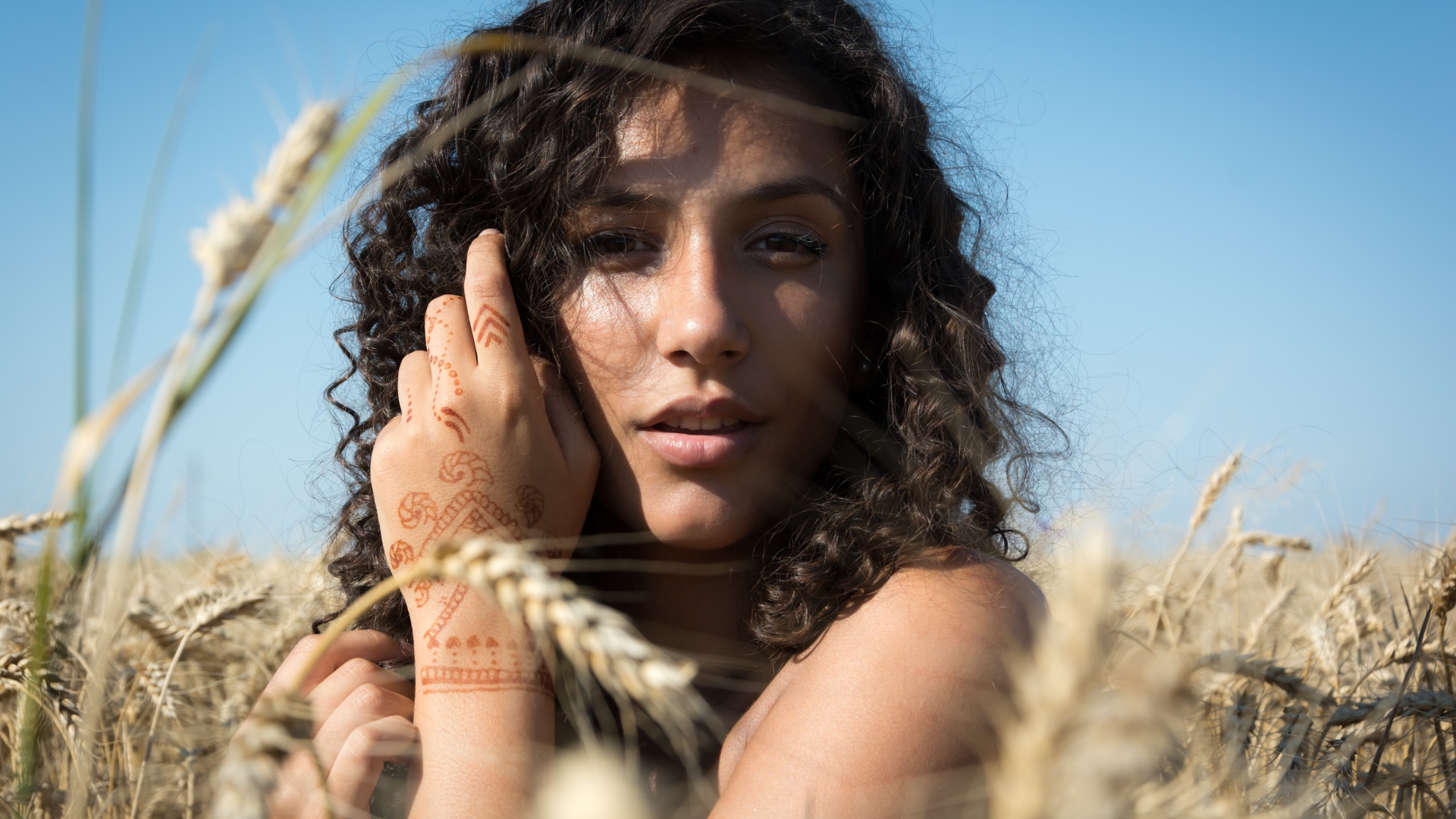 Красивая девушка с рисунком мехенди на руке на пшеничном поле 