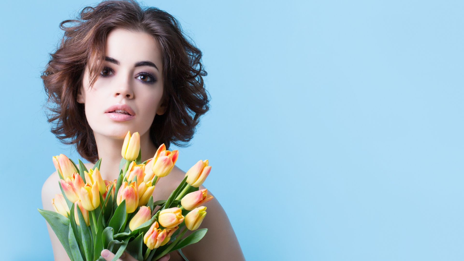 Кареглазая шатенка с букетом тюльпанов на голубом фоне
