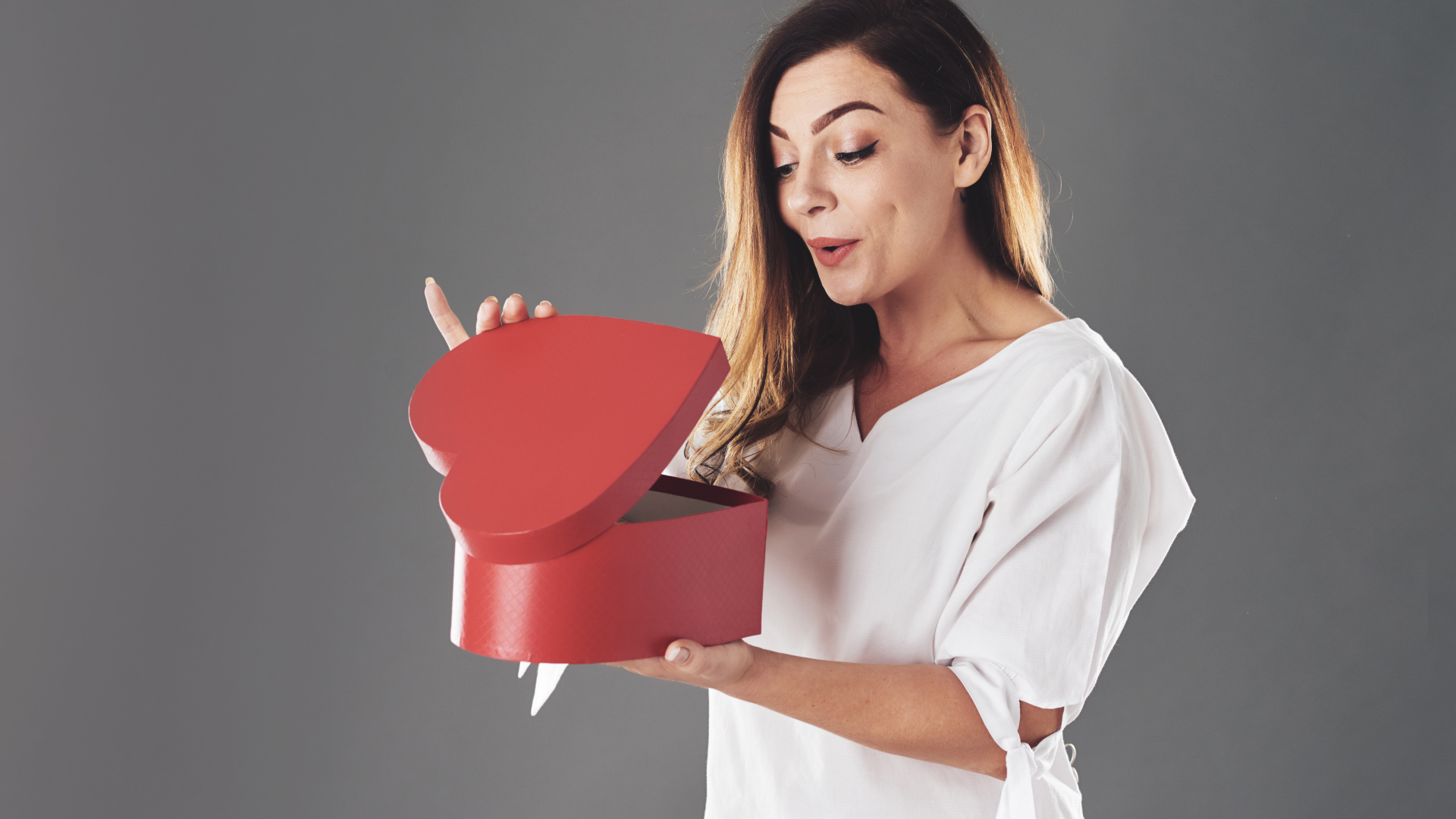 Любопытная девушка смотрит в красную коробку в форме сердца