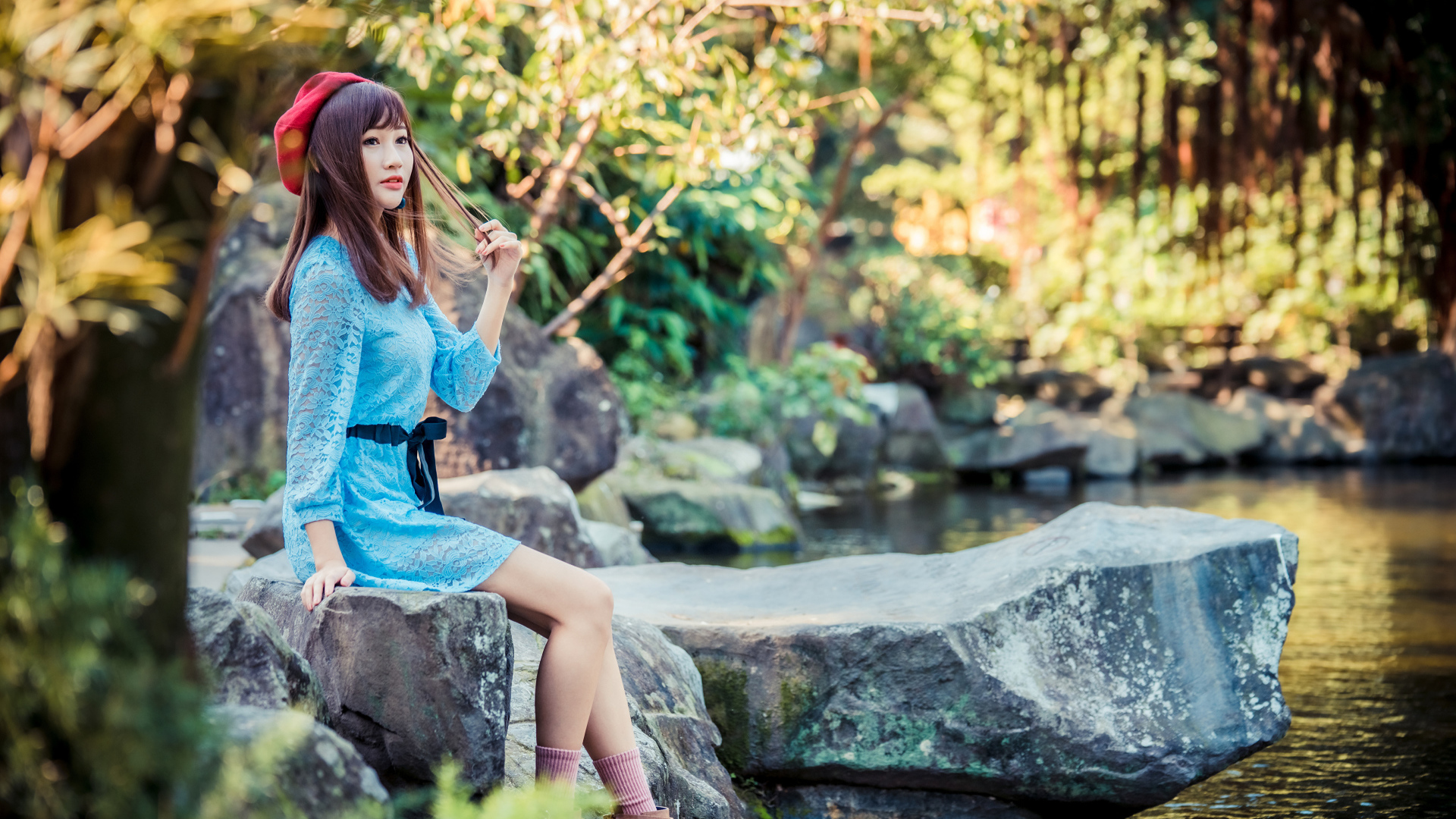 Милая азиатка в берете и синем платье сидит у воды 