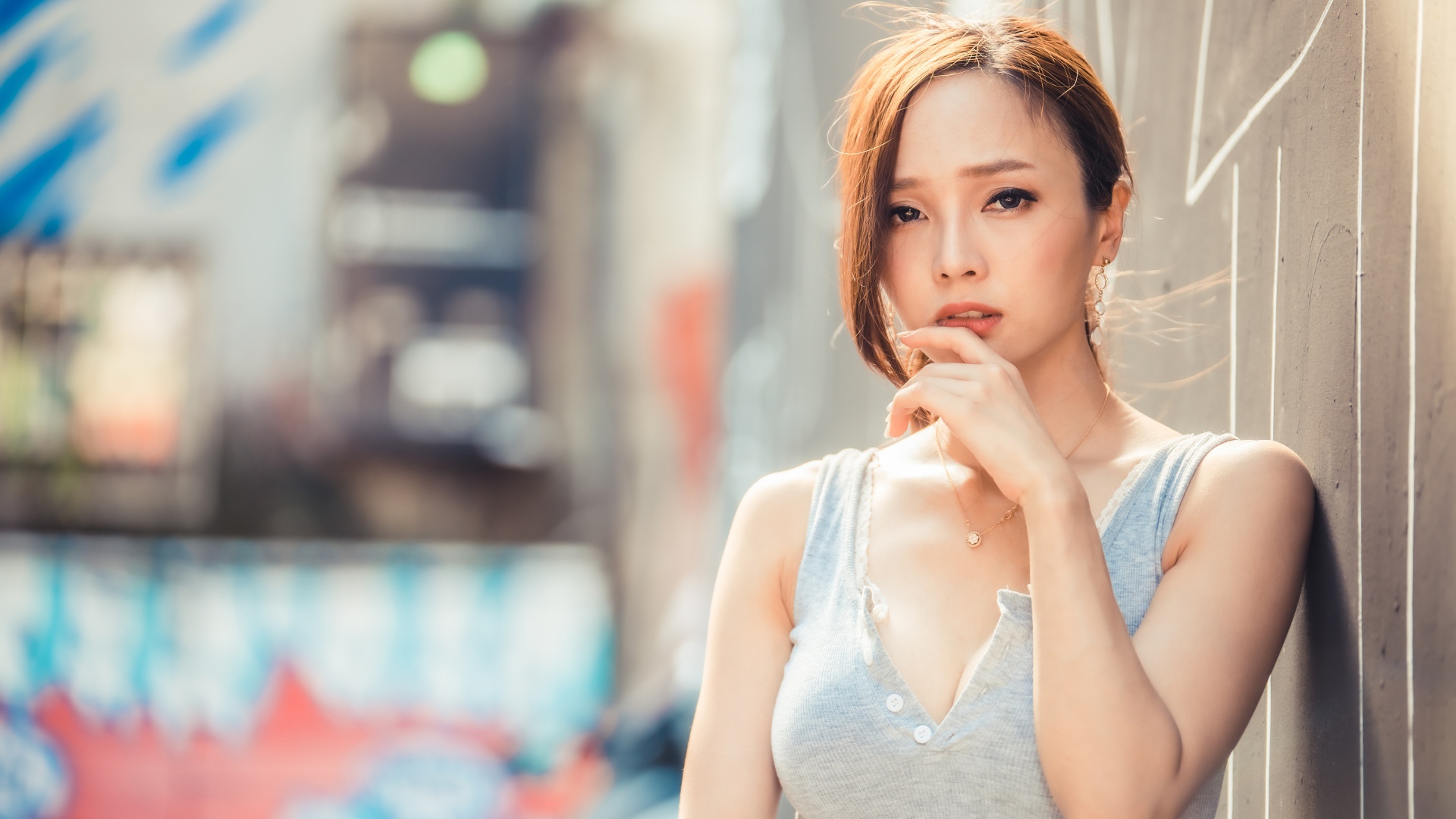 Милая девушка азиатка  с рукой у лица стоит у стены 