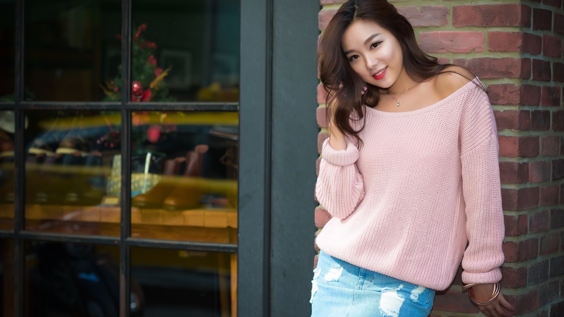 Милая азиатка в розовом свитере стоит у стены 