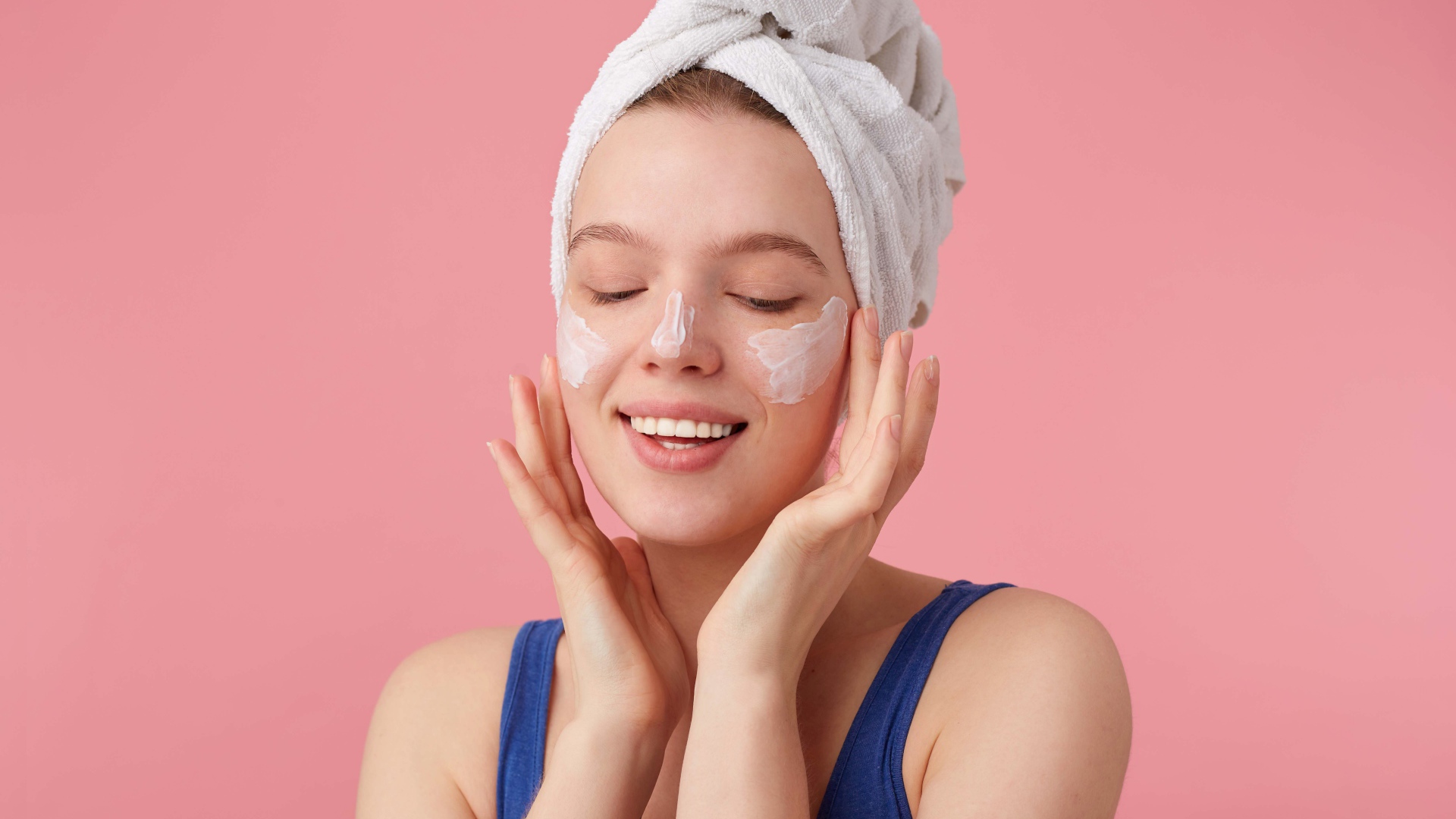 Девушка с полотенцем на голове мажет крем на лицо