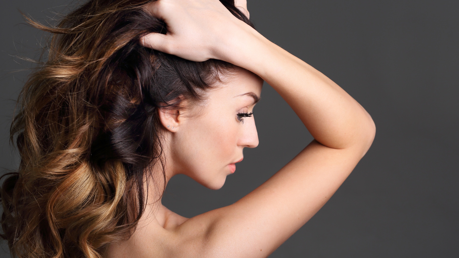 Девушка с руками в волосах на сером фоне