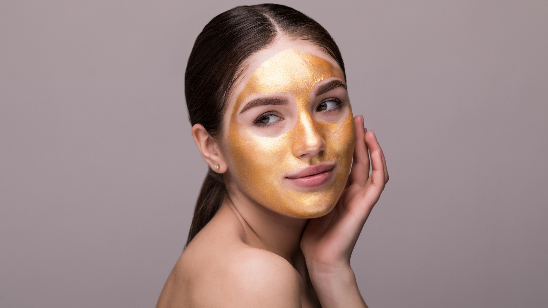 Золотая маска на лице у молодой девушки 