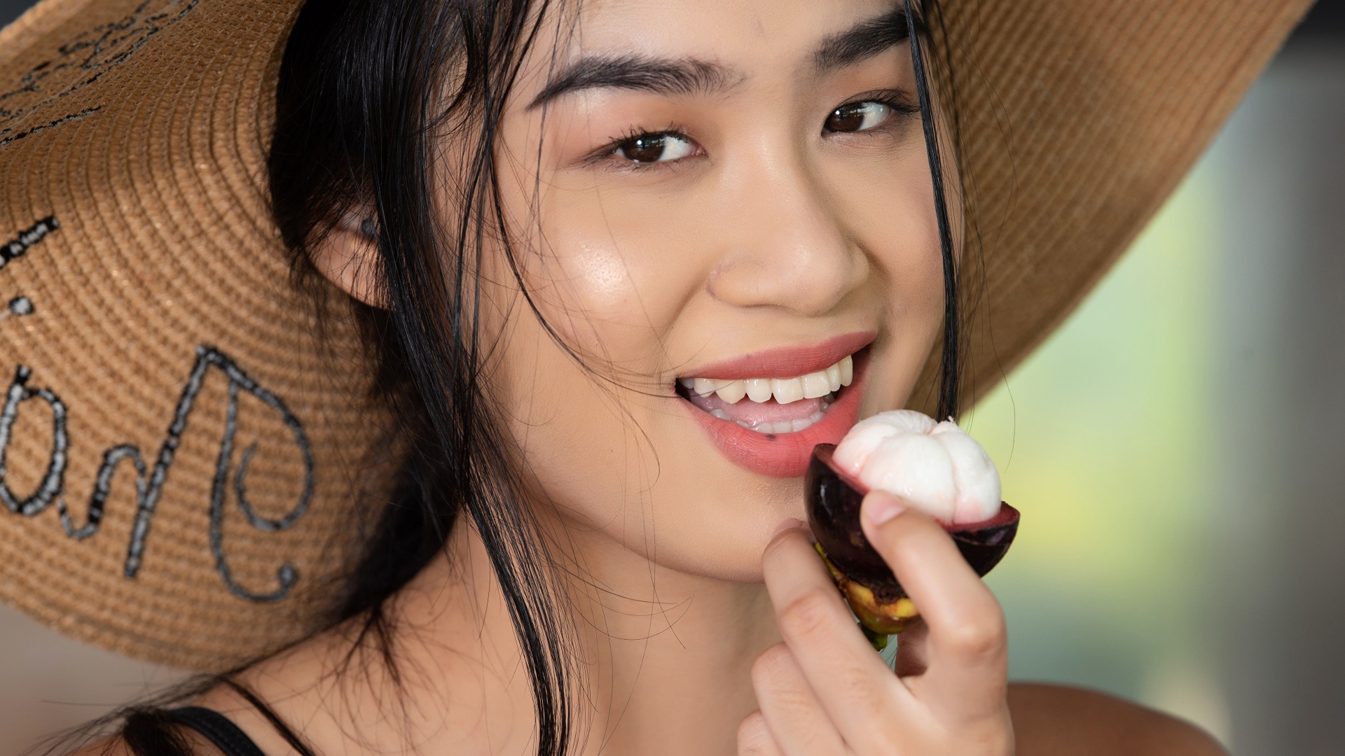 Улыбающаяся азиатка в шляпе с фруктом в руке