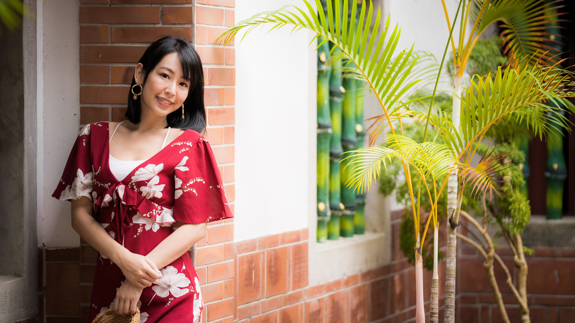 Smiling asian woman in red dress stands against the wall