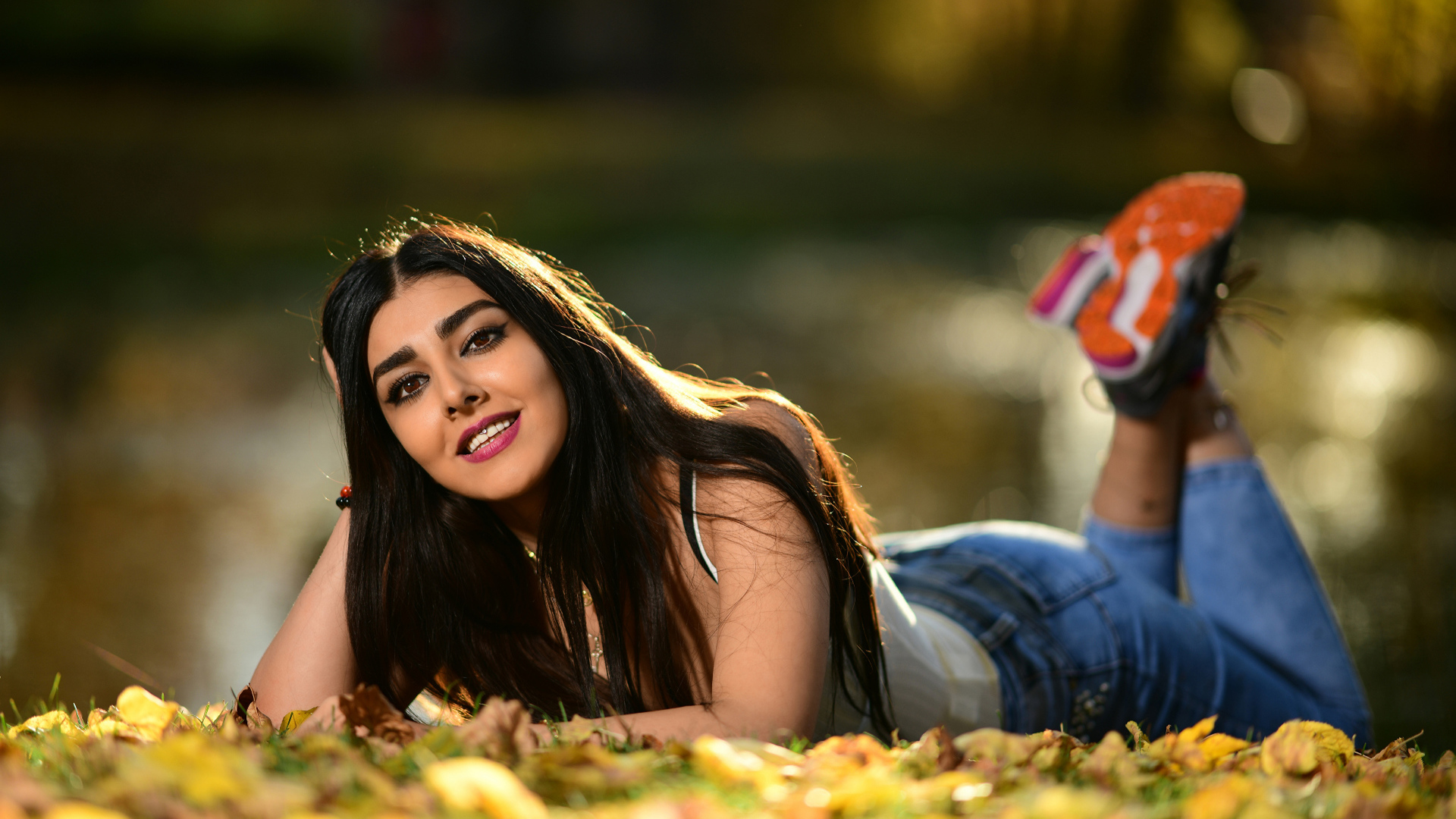 Улыбающаяся девушка модель лежит на земле с опавшими листьями