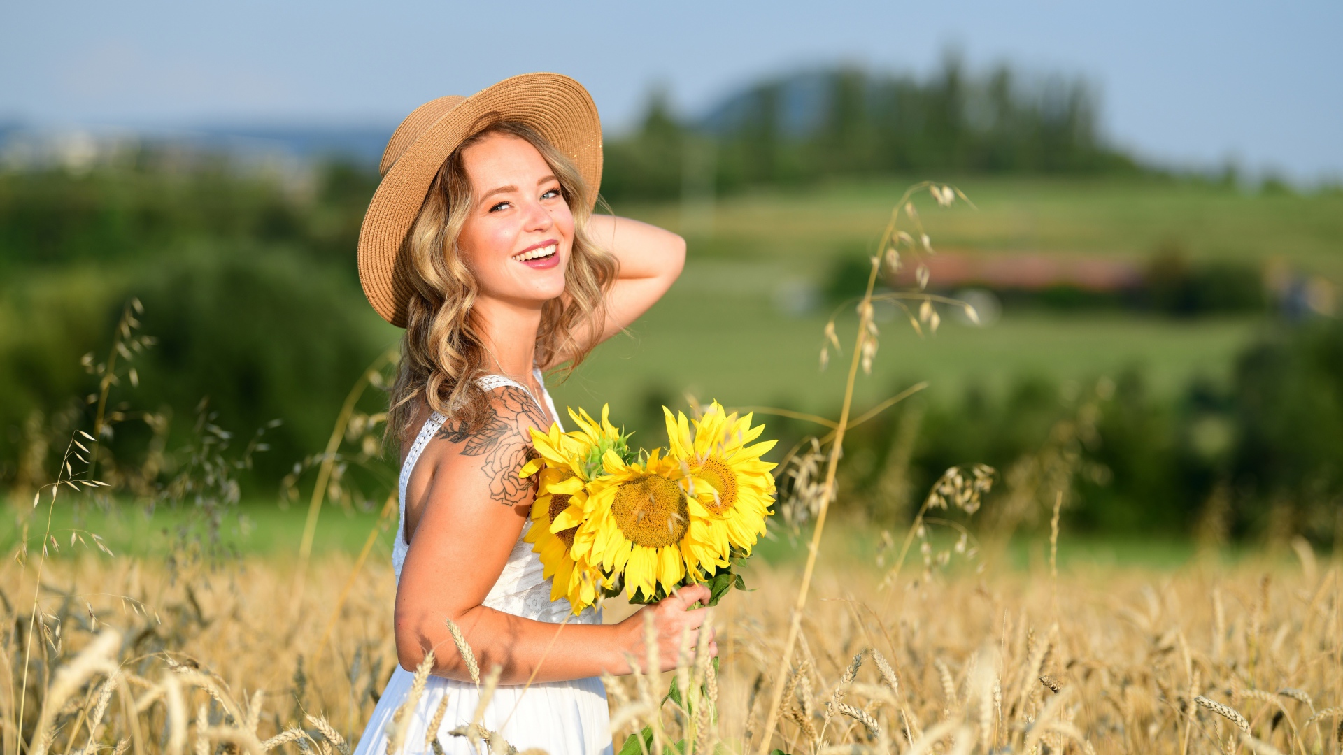 Улыбающаяся девушка с букетом подсолнухов на поле пшеницы