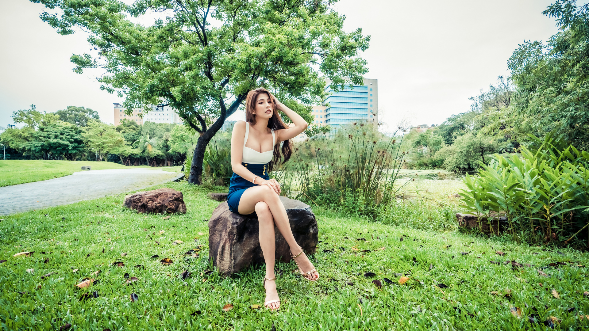 Эффектная девушка азиатка сидит на камне в парке