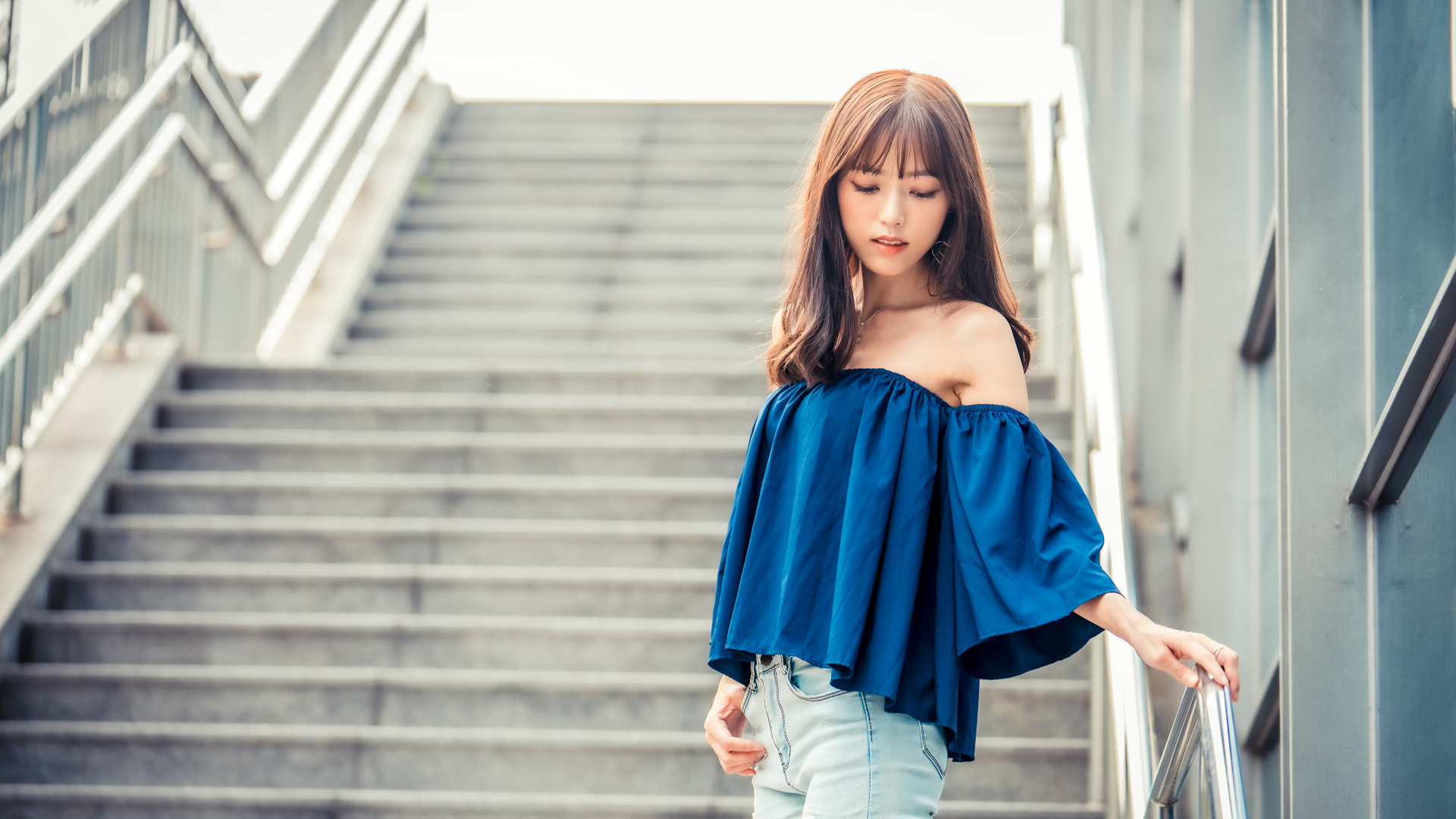 Стильная девушка азиатка с опущенной головой стоит на ступеньках 