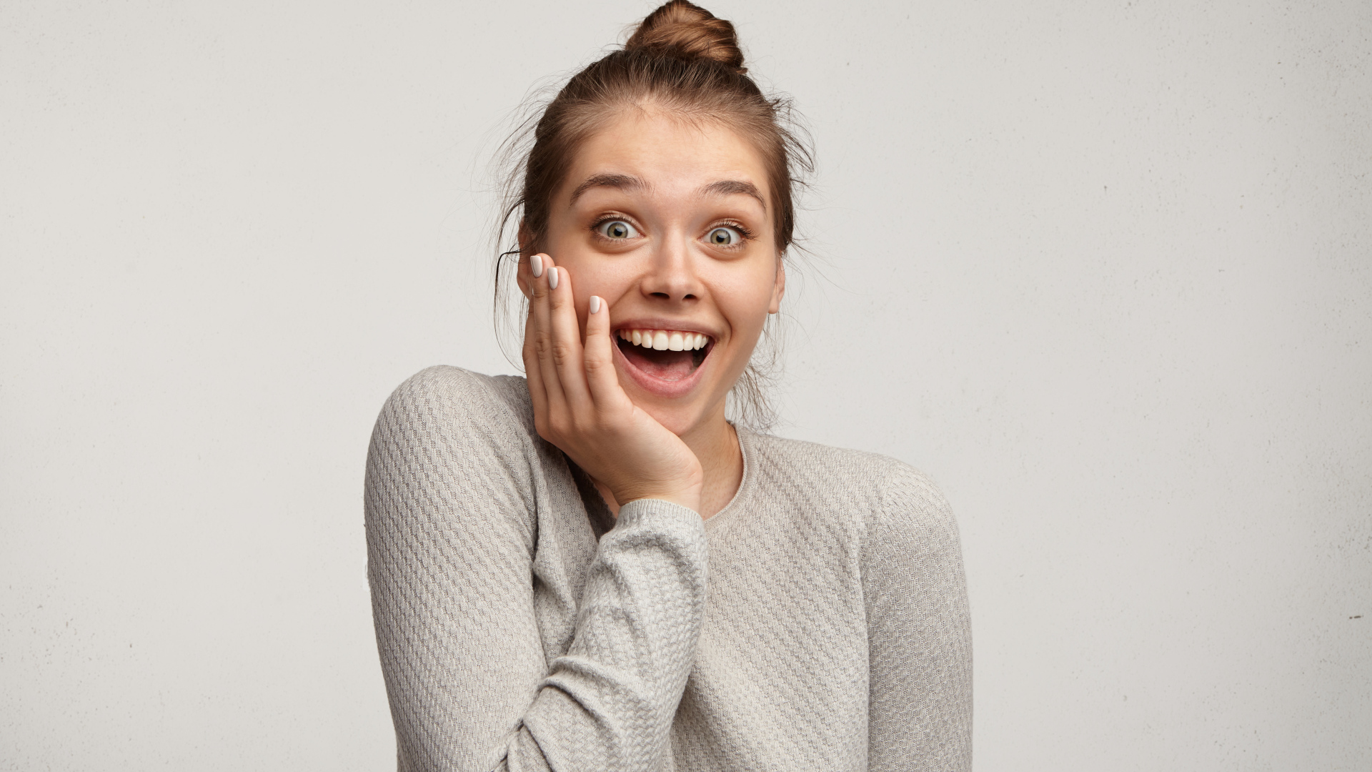 Удивленная девушка с рукой у лица на сером фоне 