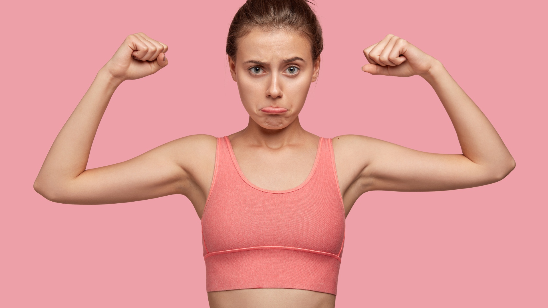 Расстроенная девушка без накаченных рук на розовом фоне