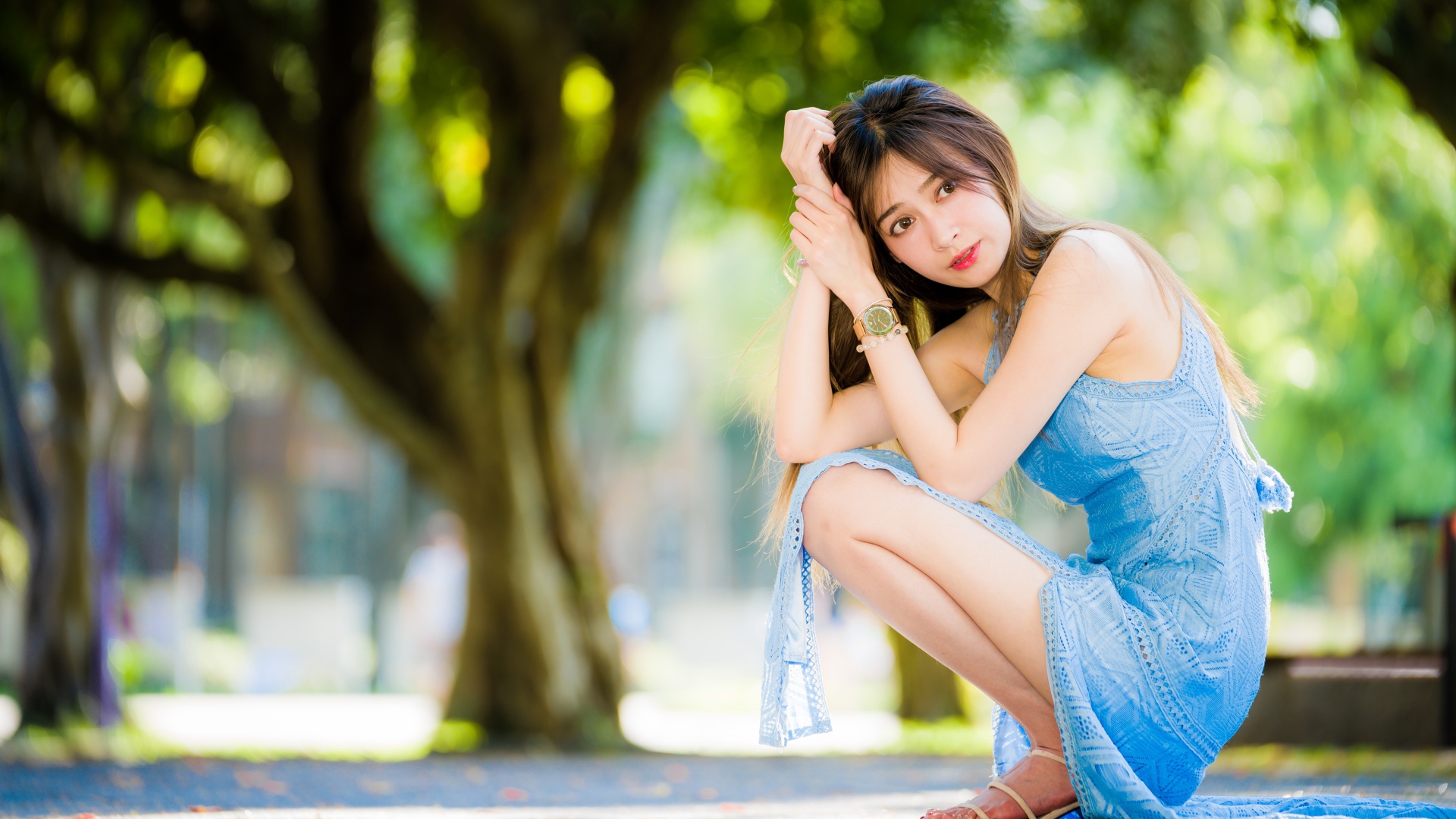 Молодая девушка азиатка в голубом платье сидит на корточках в парке 