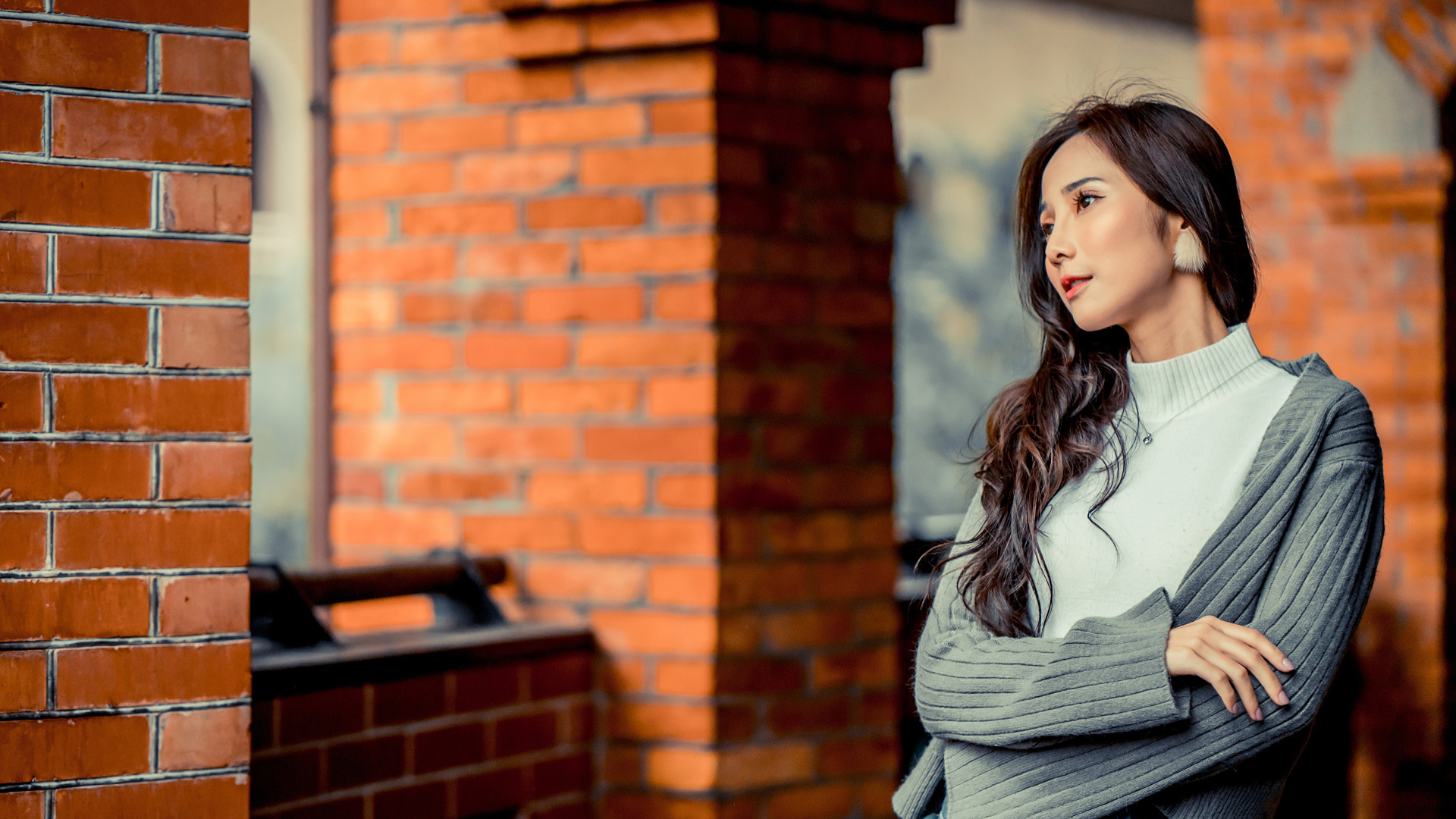 Молодая девушка азиатка в серой кофте у кирпичной стены 
