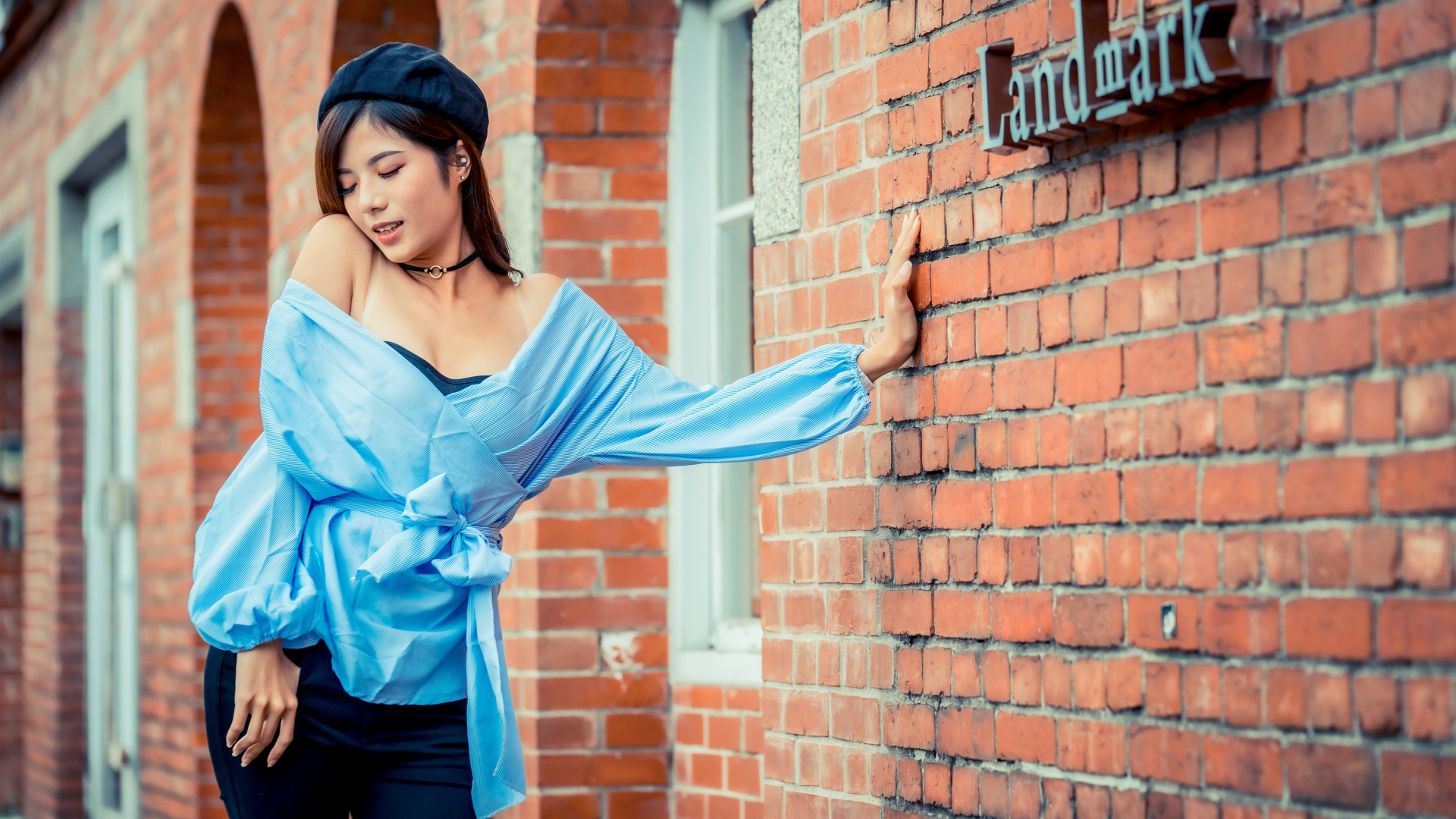 Молодая азиатка в черном берете стоит у стены 