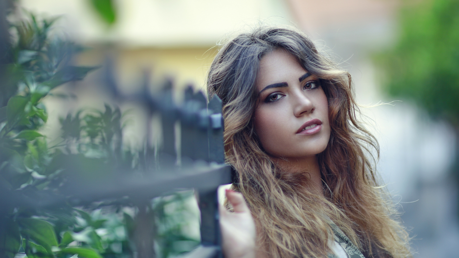 Молодая девушка с длинными волосами стоит у забора