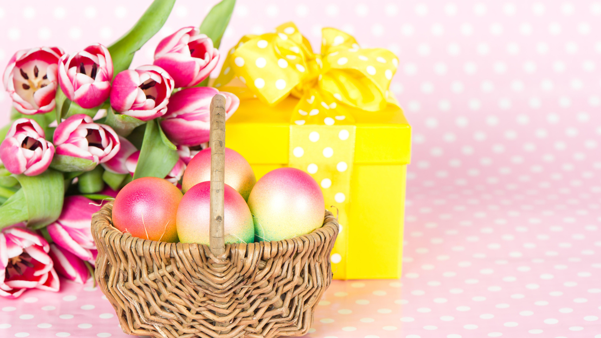 Корзина с пасхальными яйцами на столе с подарком и букетом тюльпанов 