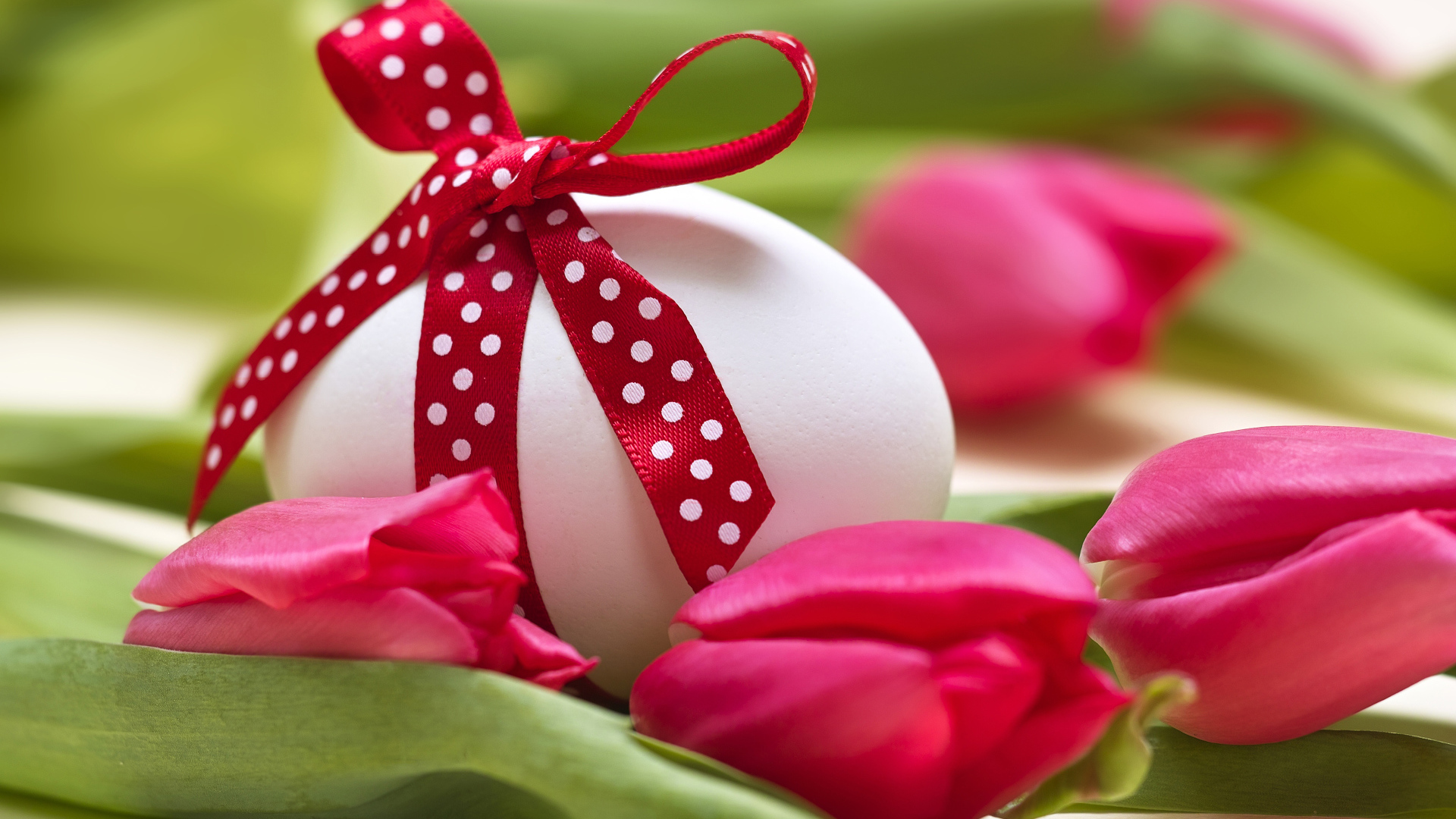 Яйцо с бантом на столе с тюльпанами на праздник Пасха