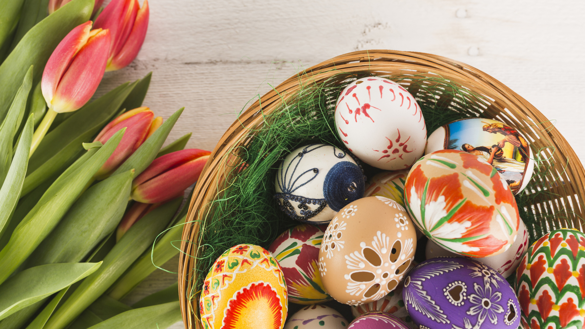 Разноцветные крашеные яйца в корзине с букетом тюльпанов на Пасху