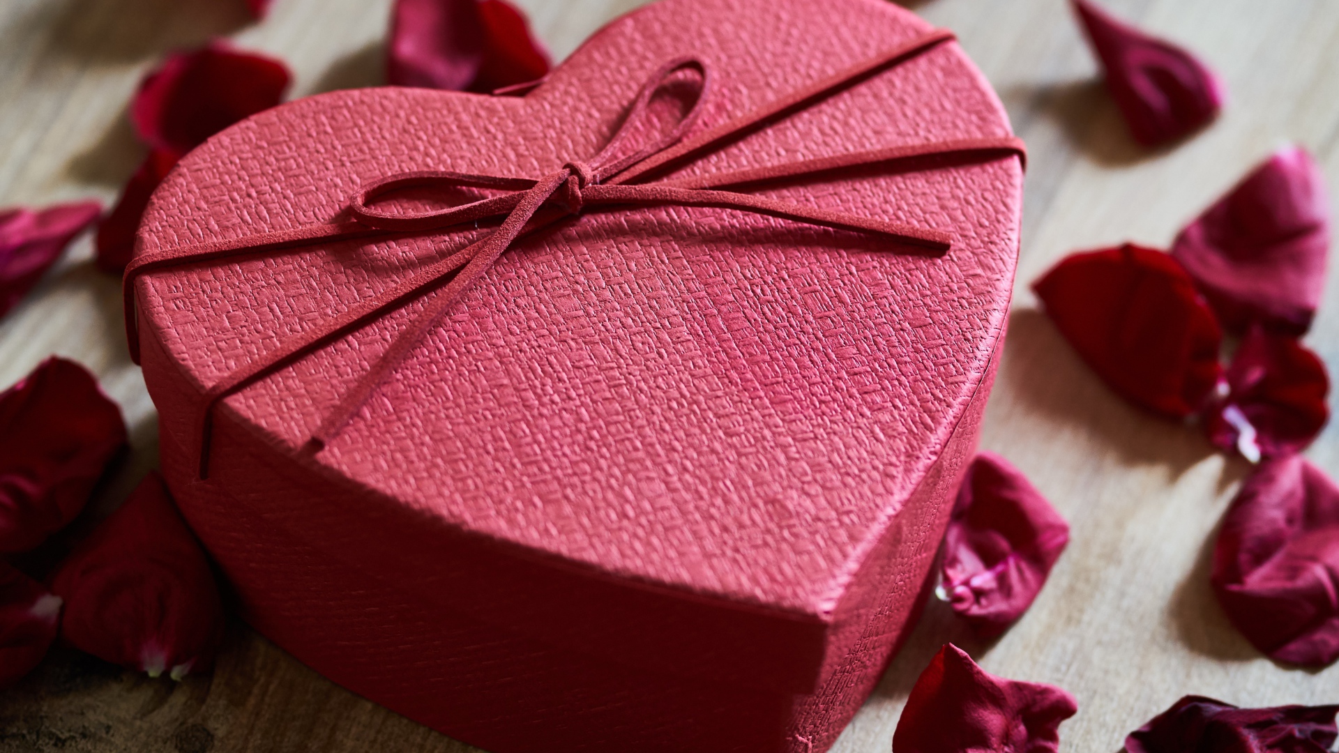 Большая красная коробка в форме сердца на столе с лепестками роз