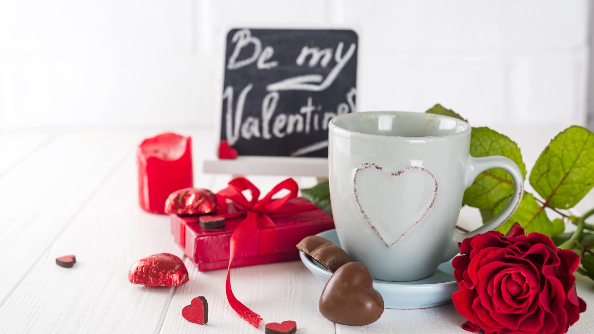 Белая чашка с конфетами и красной розой на столе в подарок на 14 февраля