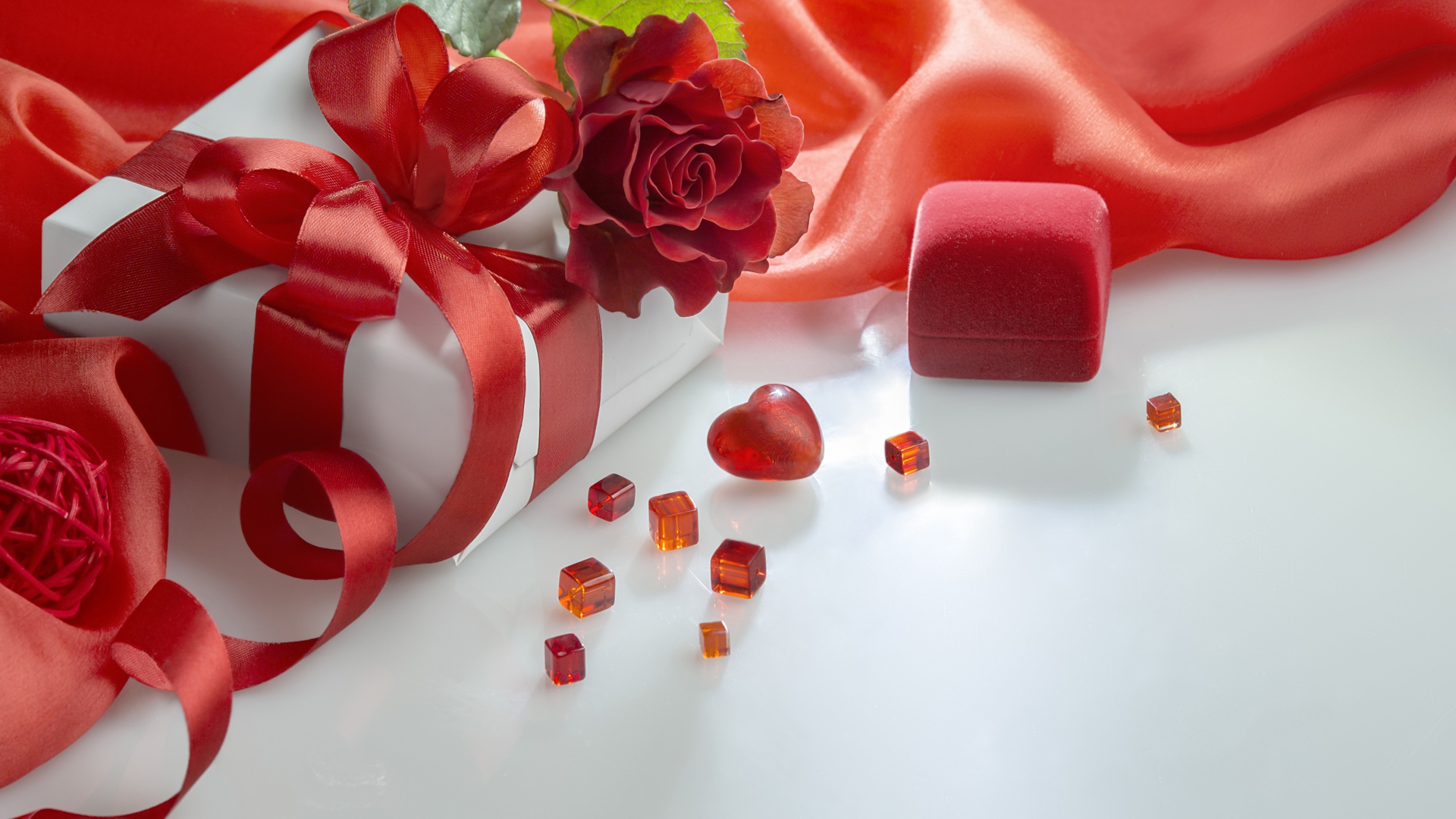 Подарки на белом столе с розой и красной тканью