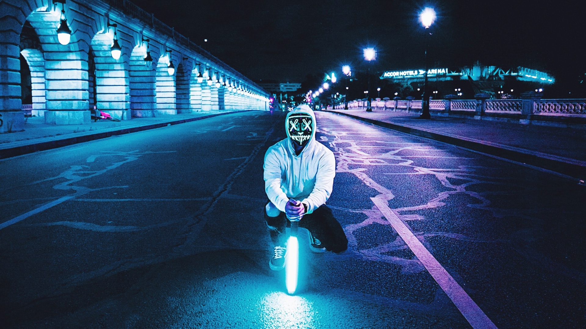 Парень в светящейся маске сидит с неоновой лампой на дороге