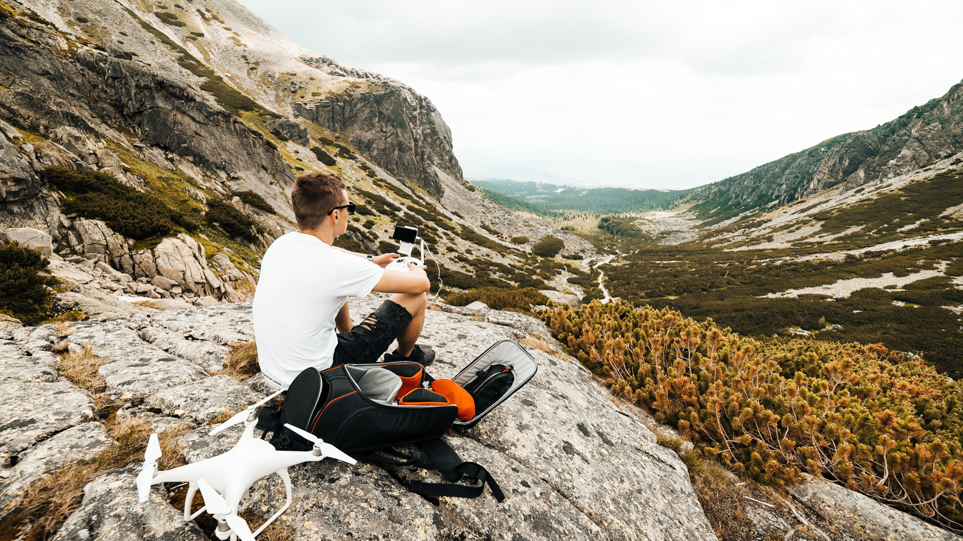 Парень с квадрокоптером сидит на камне в горах 