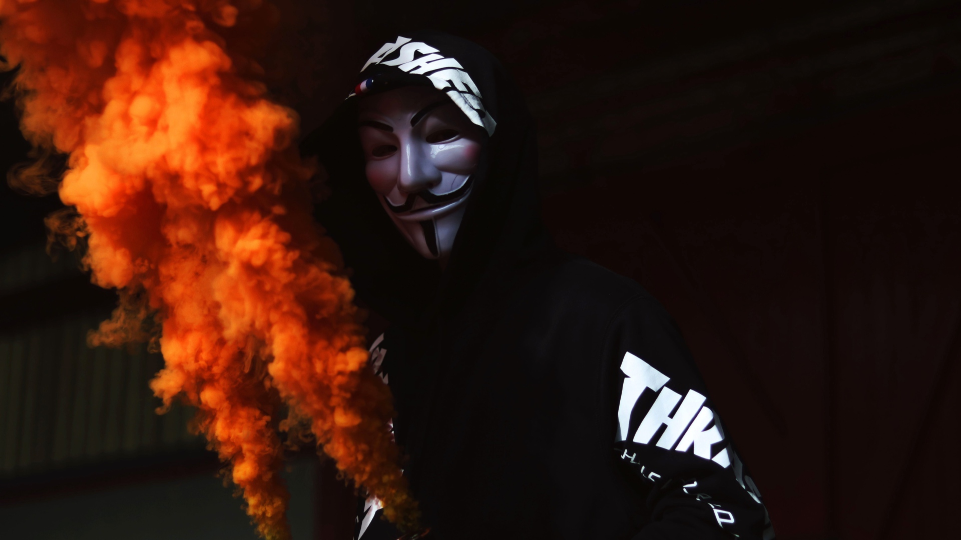 A man in an anonymous mask with a smoke bomb in his hand
