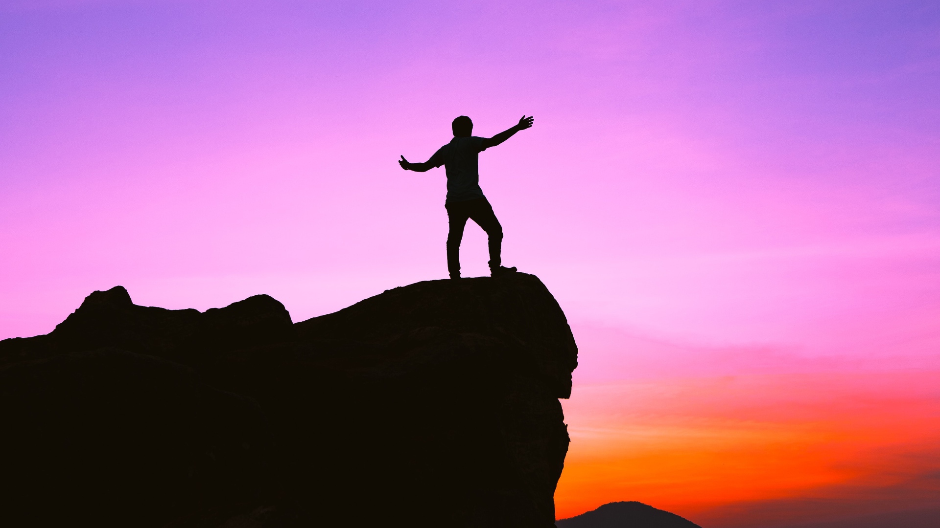 Мужчина стоит на краю утеса на закате