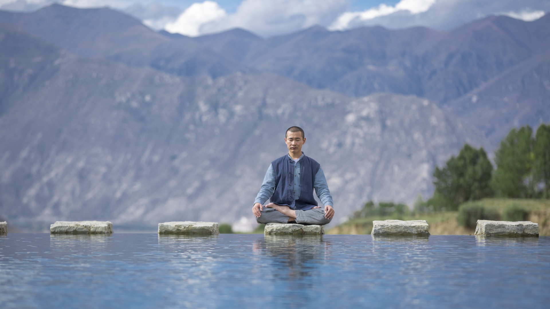 Asian man in lotus position meditates by the water.