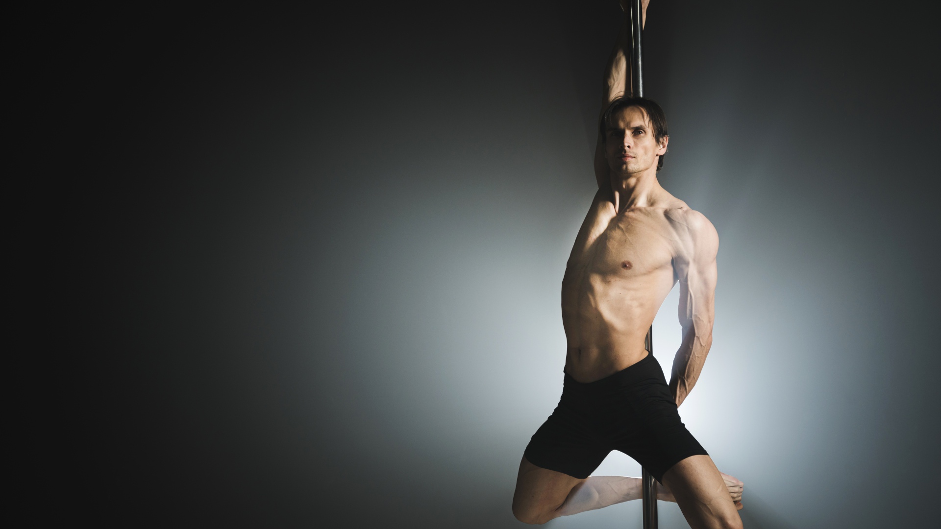 Мужчина танцует на пилоне на сером фоне