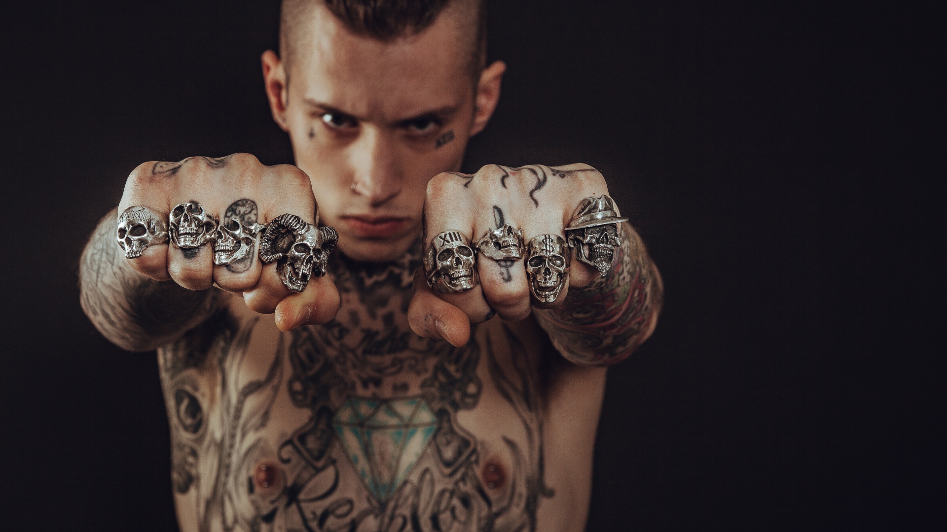 Мужчина с татуировками на теле с перстнями на пальцах