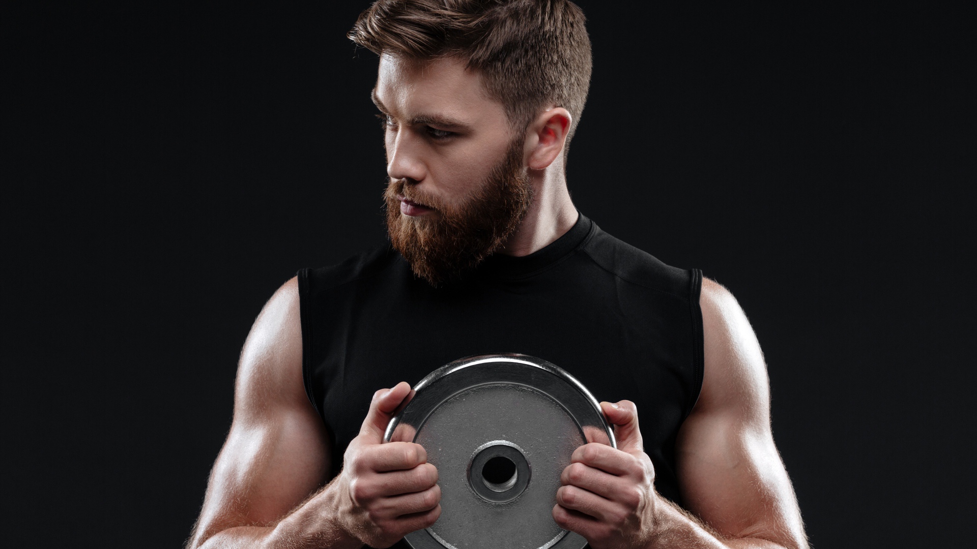 Молодой накаченный парень с железным диском на черном фоне