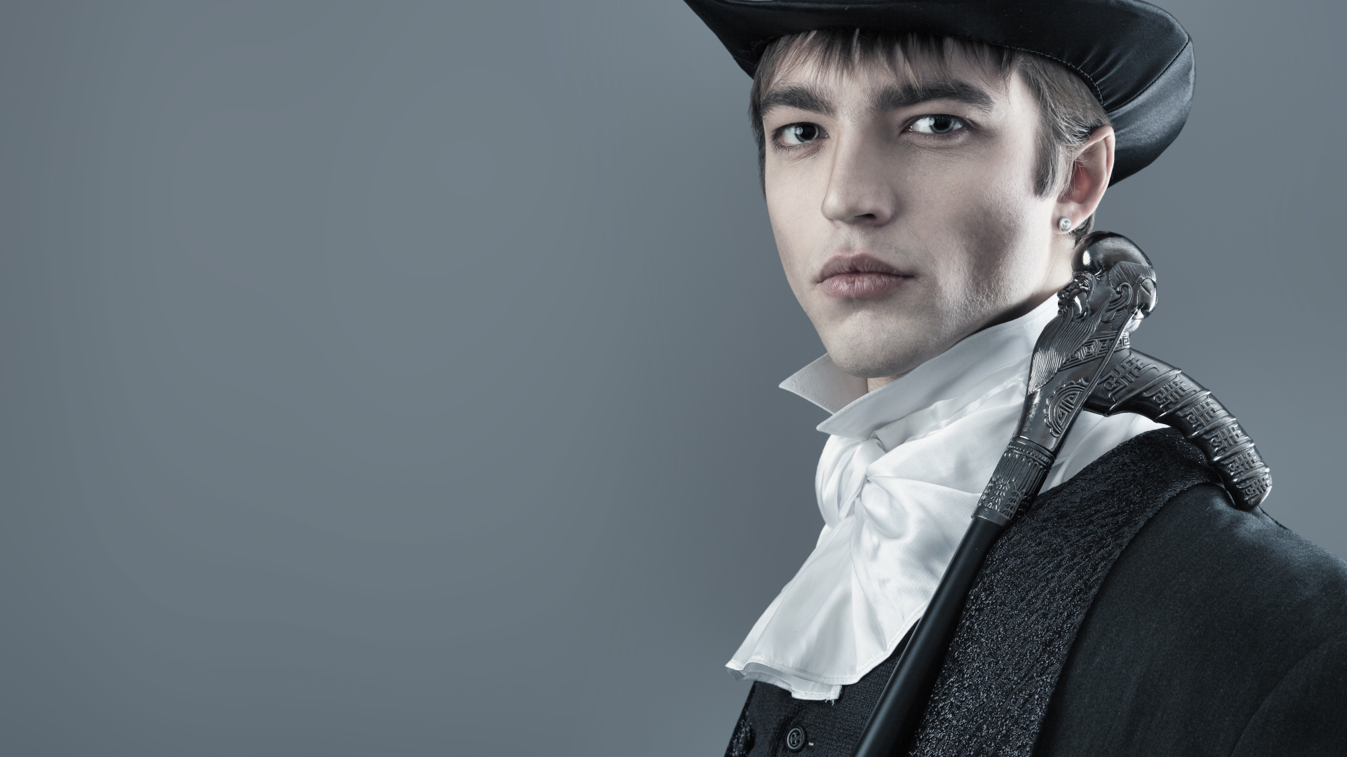 Красивый молодой человек в черном цилиндре и фраке на сером фоне