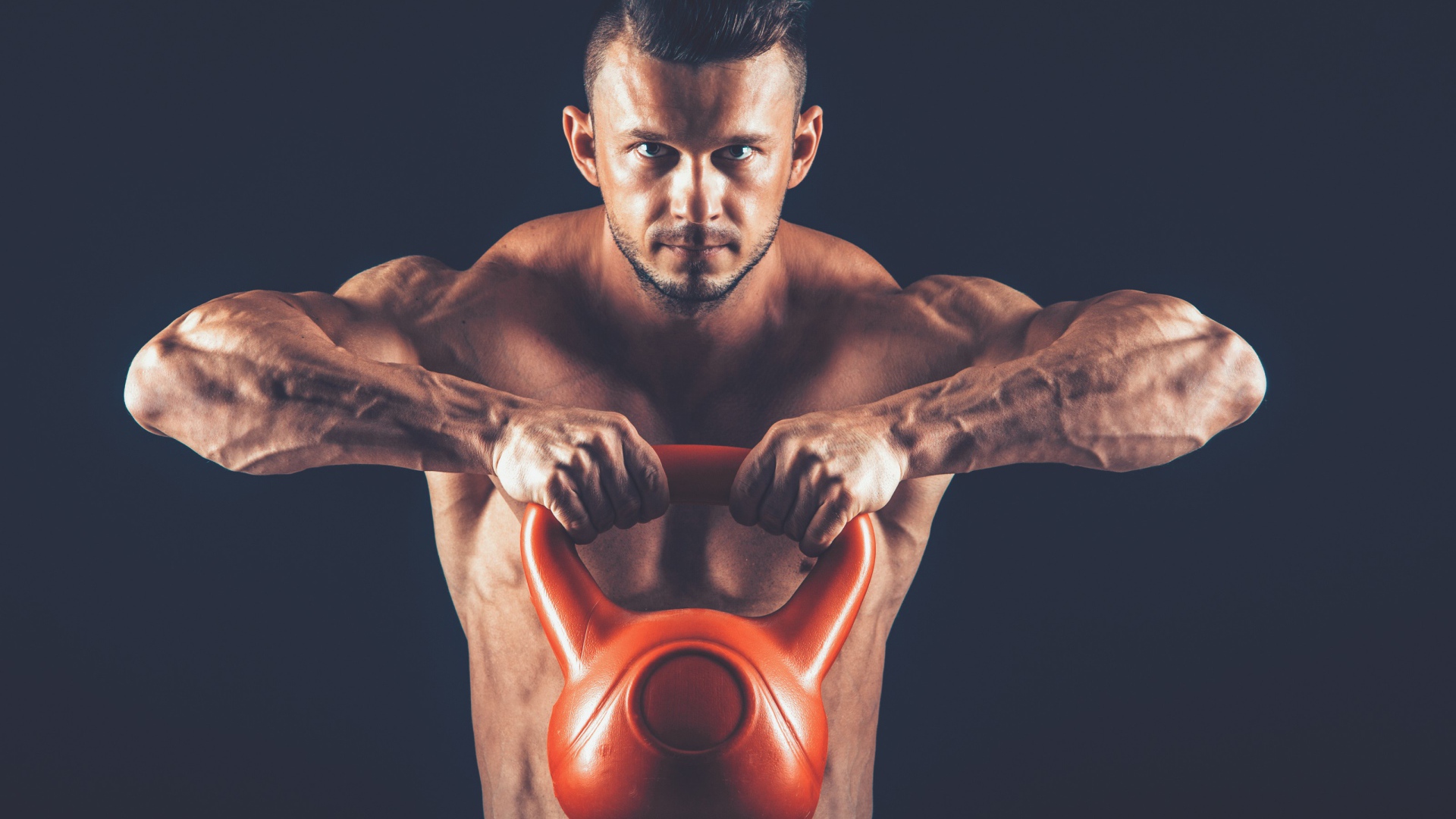 Накаченный парень поднимает тяжелую гирю на черном фоне