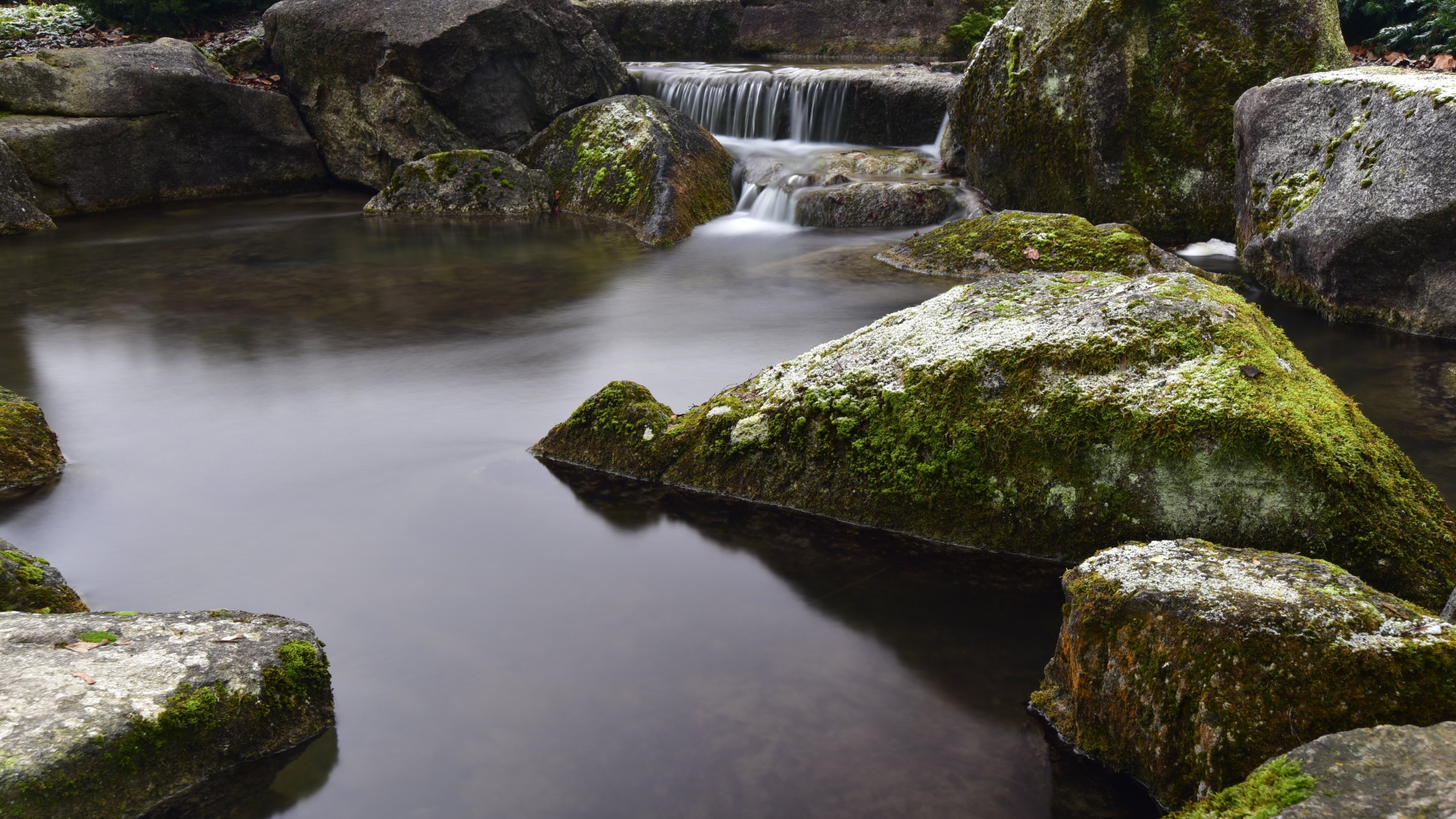 Вода стекает по камням в пруд с большими покрытыми мхом камнями
