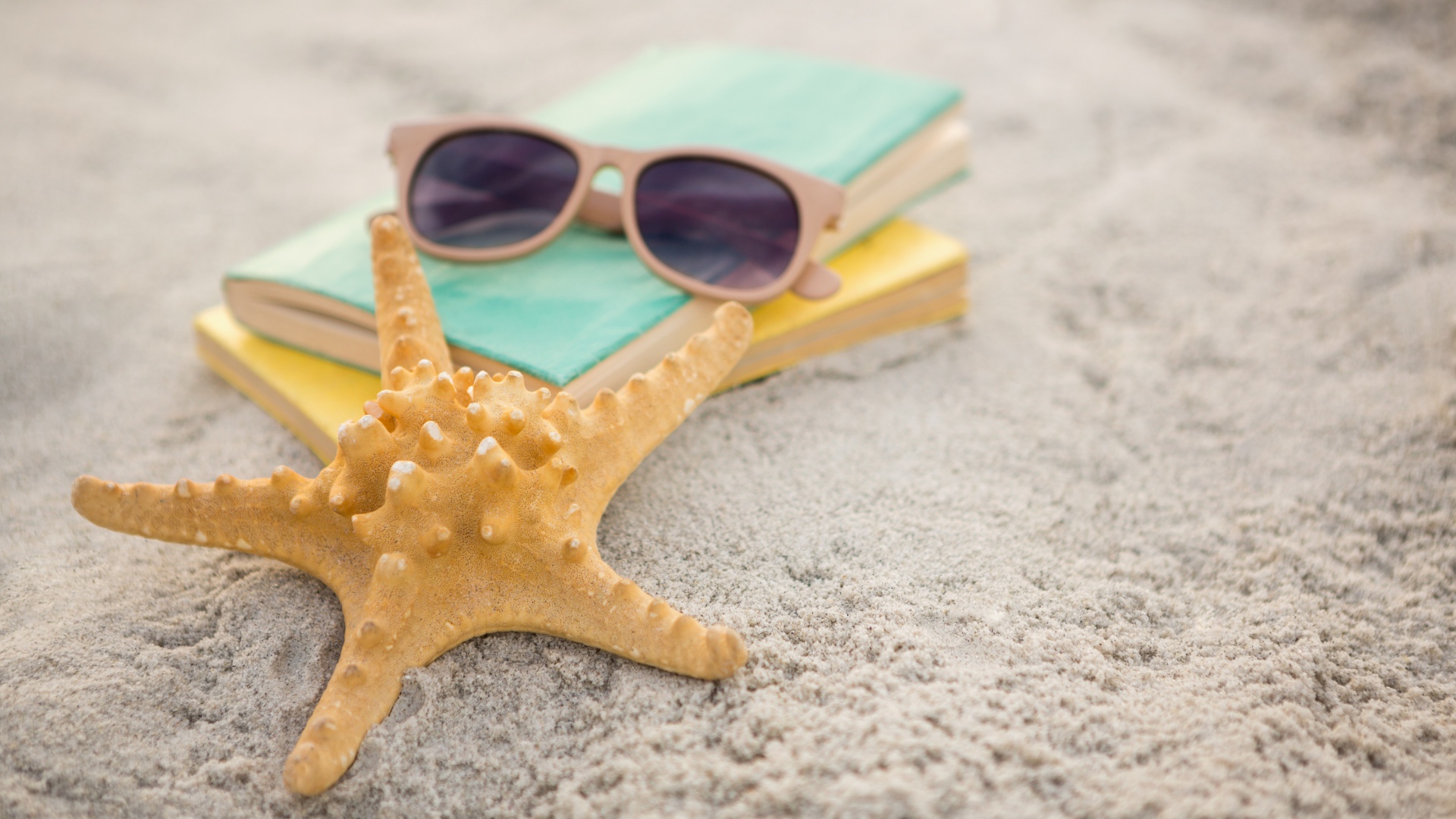 Книги, очки и морская звезда на белом песке 